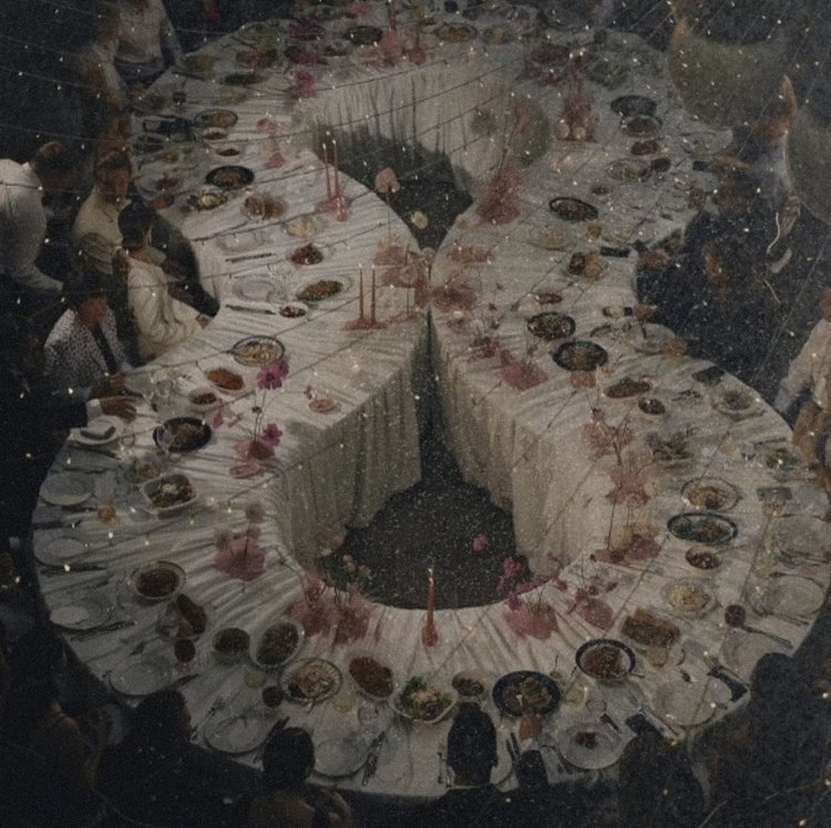 U-shaped banquet table with white tablecloths, decorated with food and pink floral arrangements, surrounded by people.