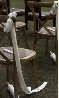 Wedding ceremony chairs with white ribbons and umbrellas on grass