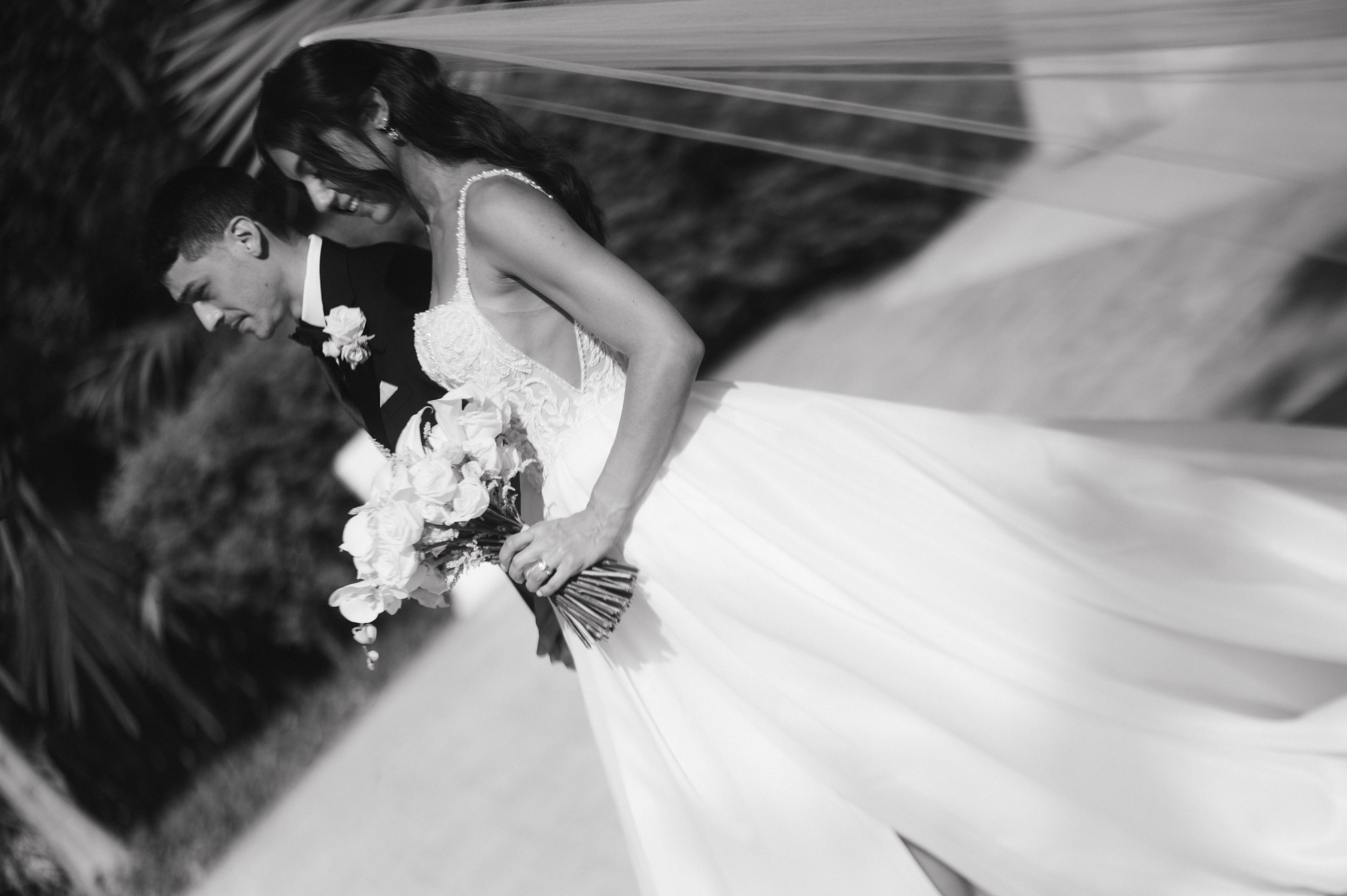 Black and white photo of a happy bride and groom on their wedding day, smiling and leaning towards each other, with the bride holding a bouquet of flowers.