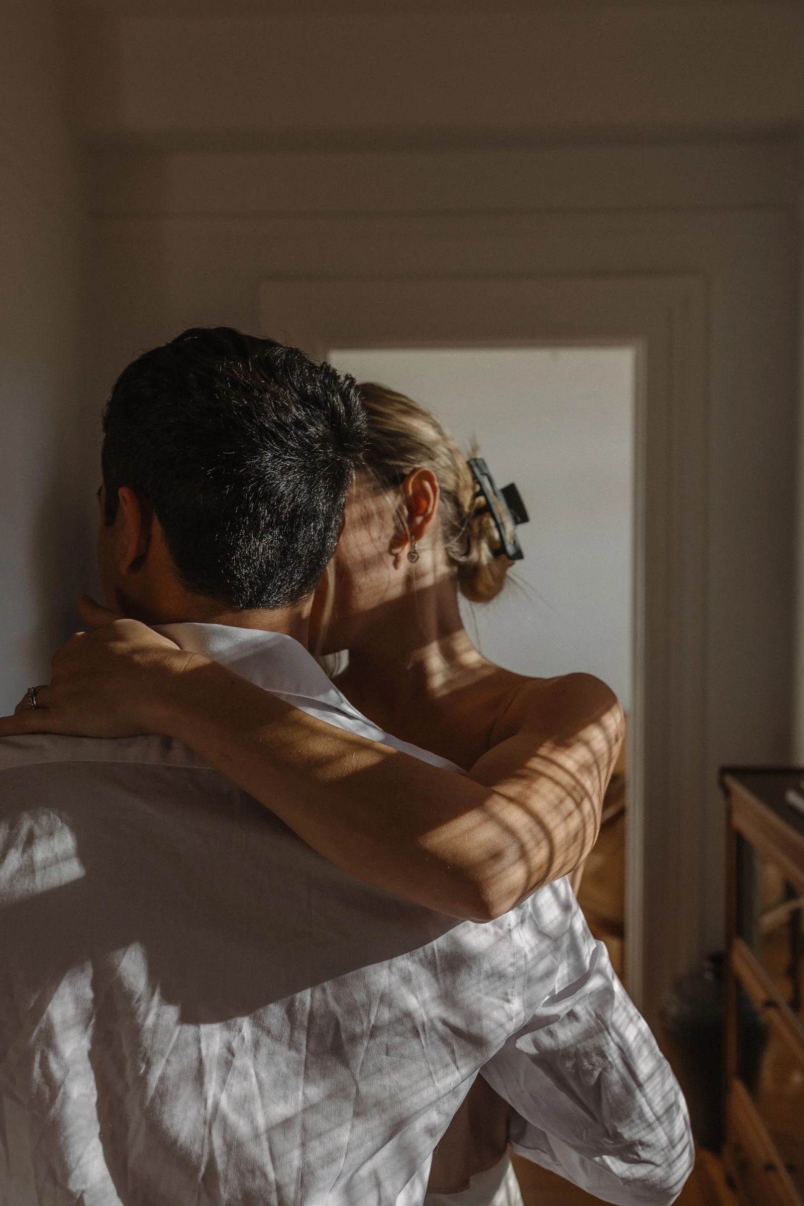 A couple embracing each other in a room with sunlight casting shadows on their faces and bodies.