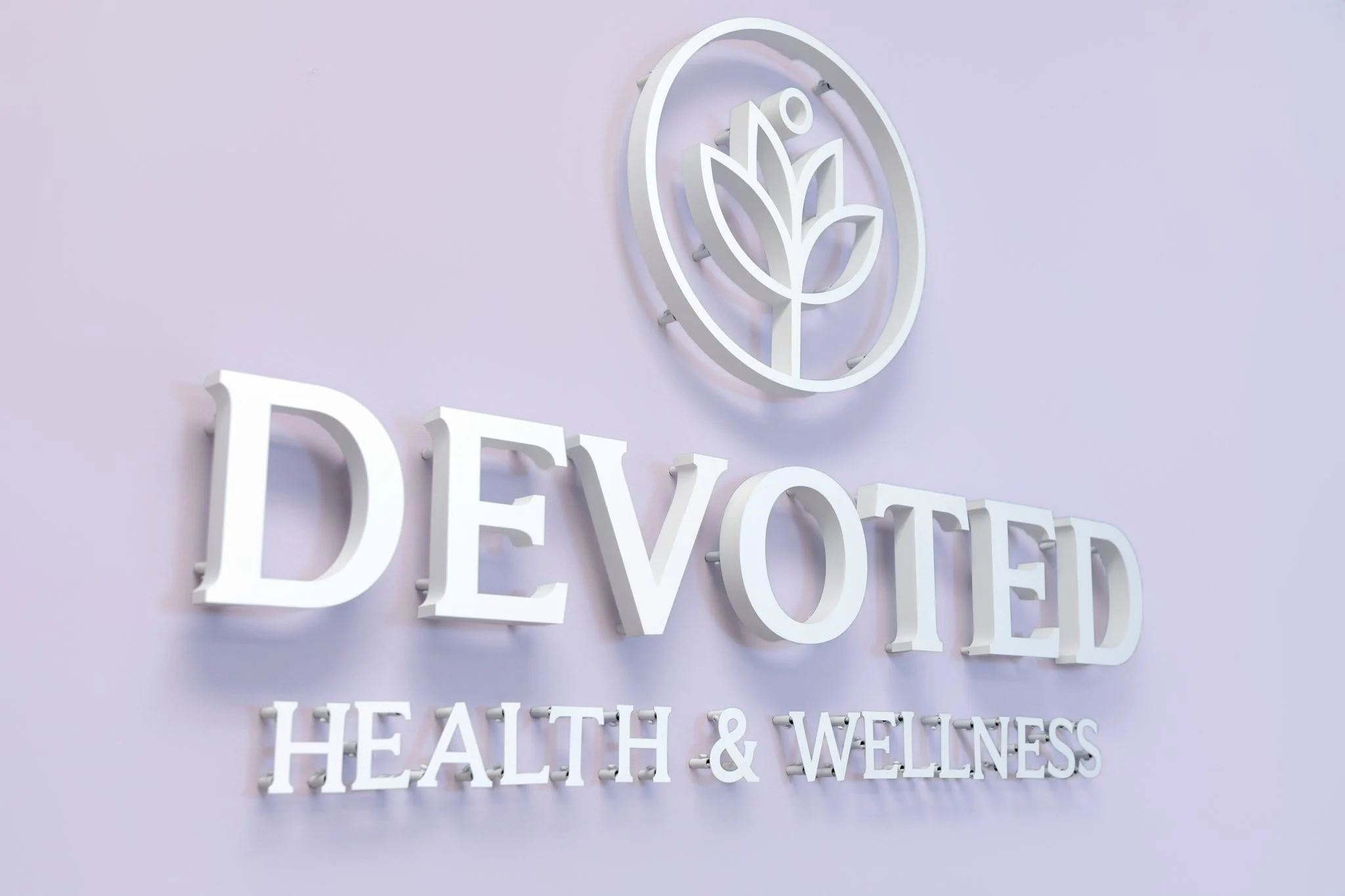 Sign with a leaf logo and the words 'Devoted' and 'Health & Wellness' on a purple wall.