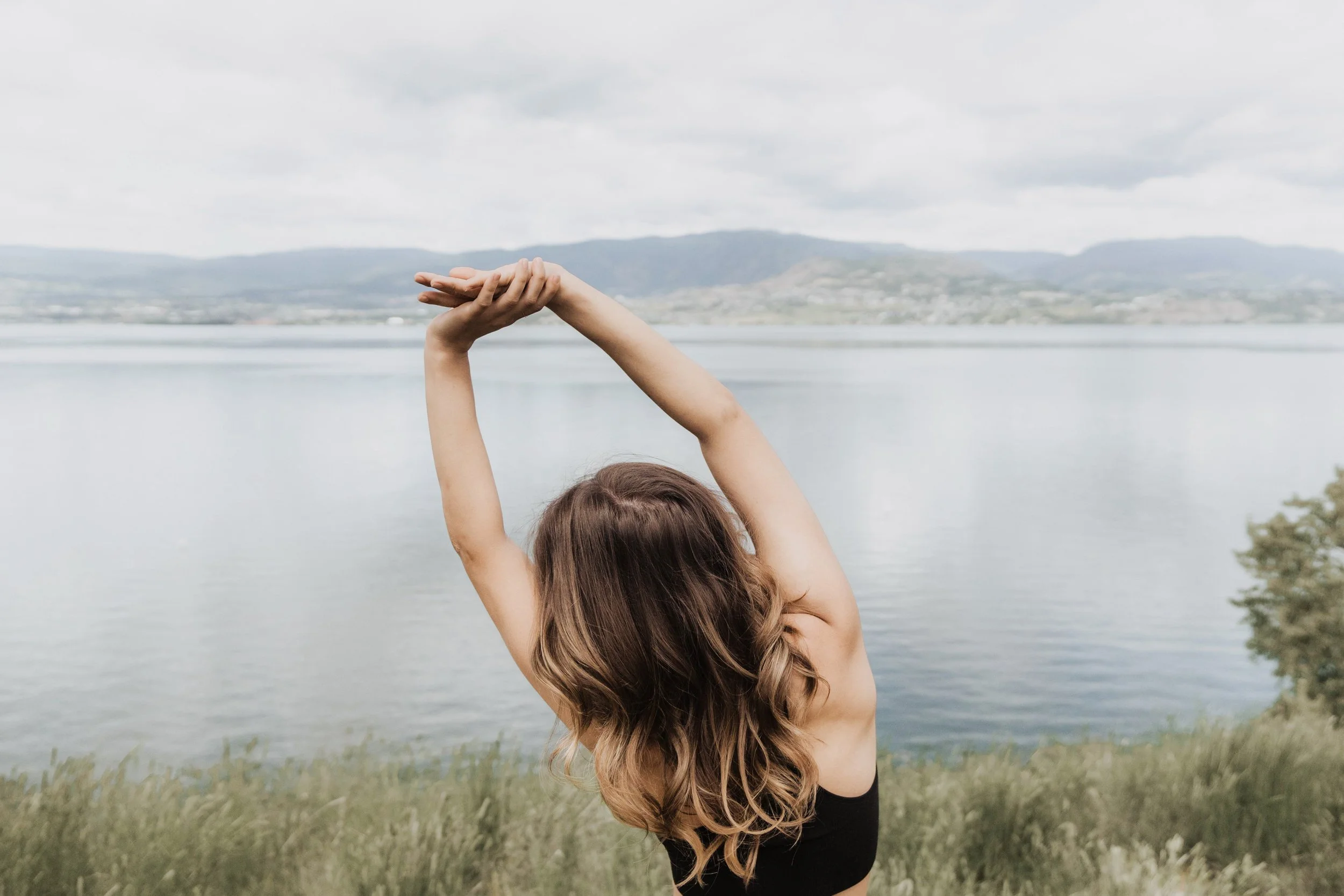 A woman with brown hair stretching in front of a lake.