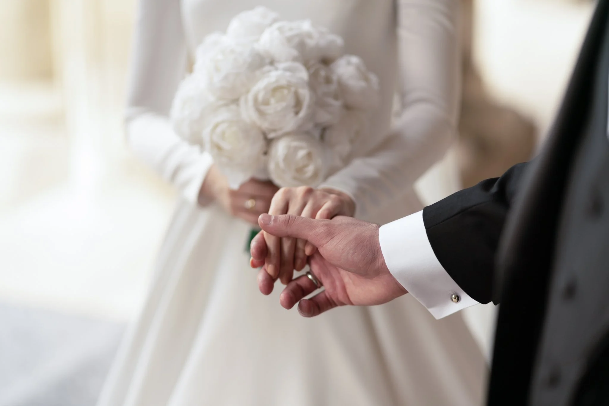Close-up of a wedding couple holding hands beside a white bridal bouquet inside San Francisco City Hall.