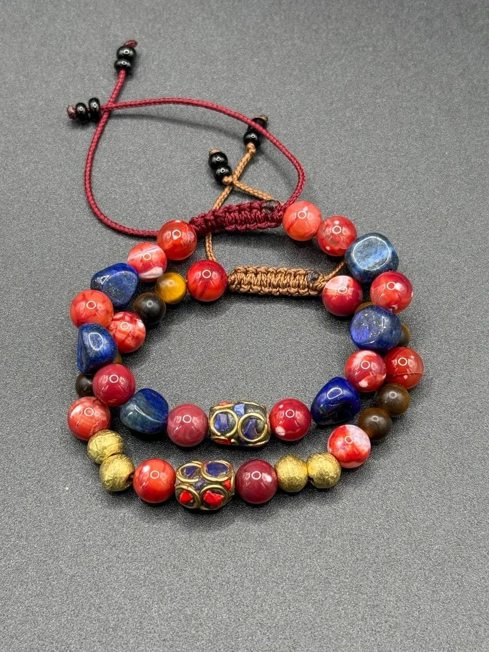 Three beaded necklaces with red, blue, gold, and black beads lying on a black surface.