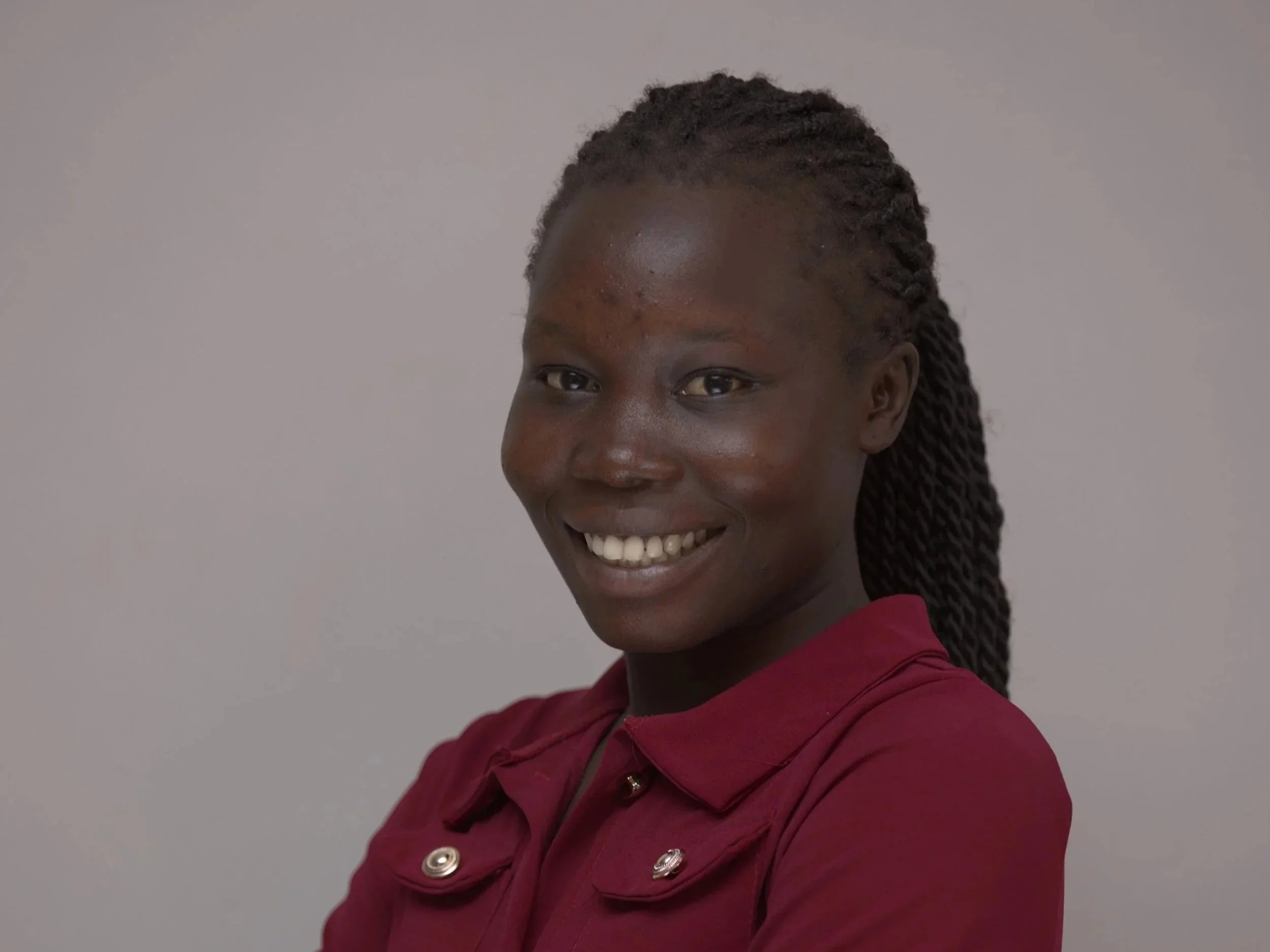 A man with glasses smiling, wearing a red and blue checkered shirt, standing against a plain light gray background.