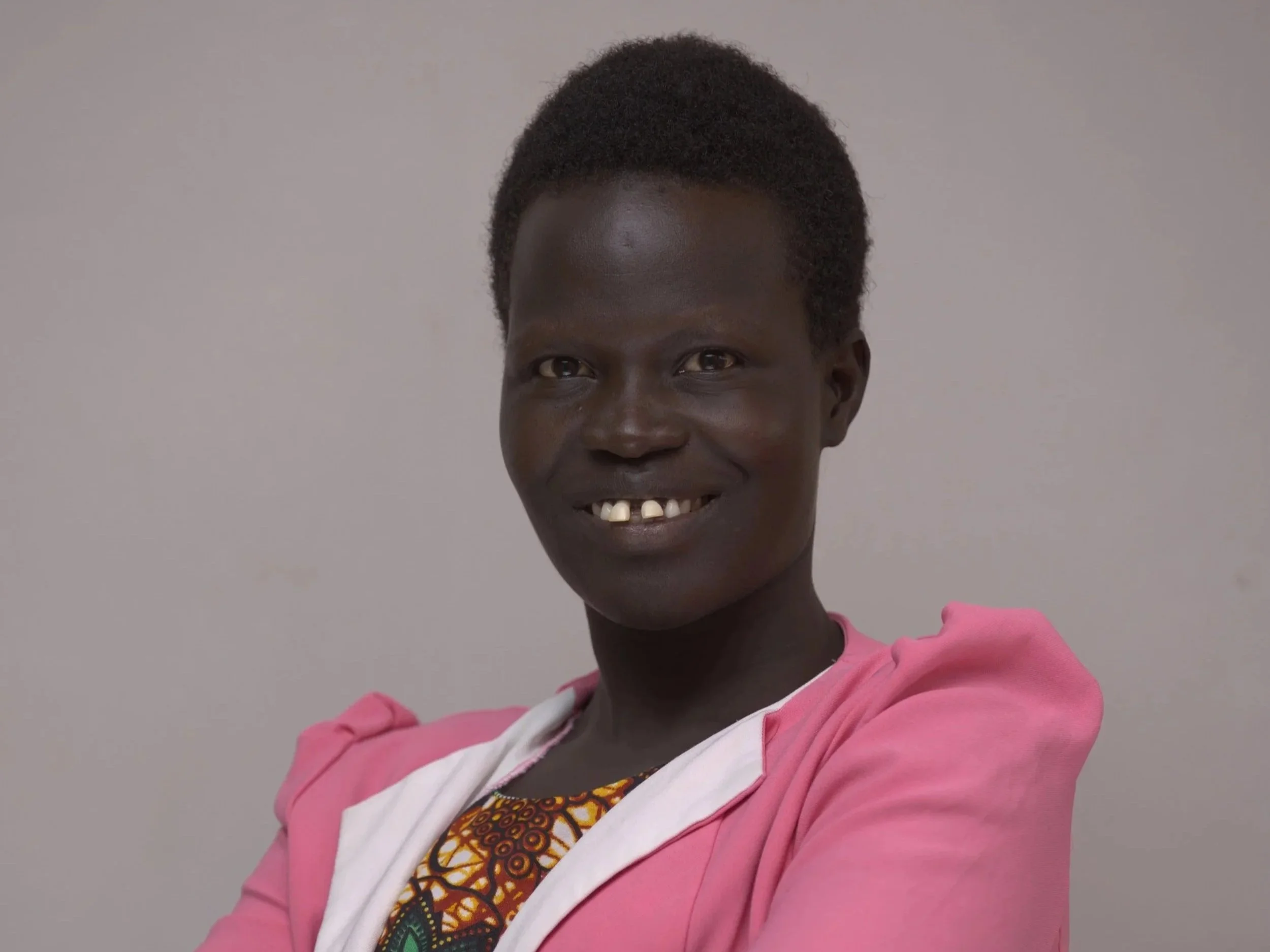Photo of a smiling woman with curly red hair, wearing a white top.