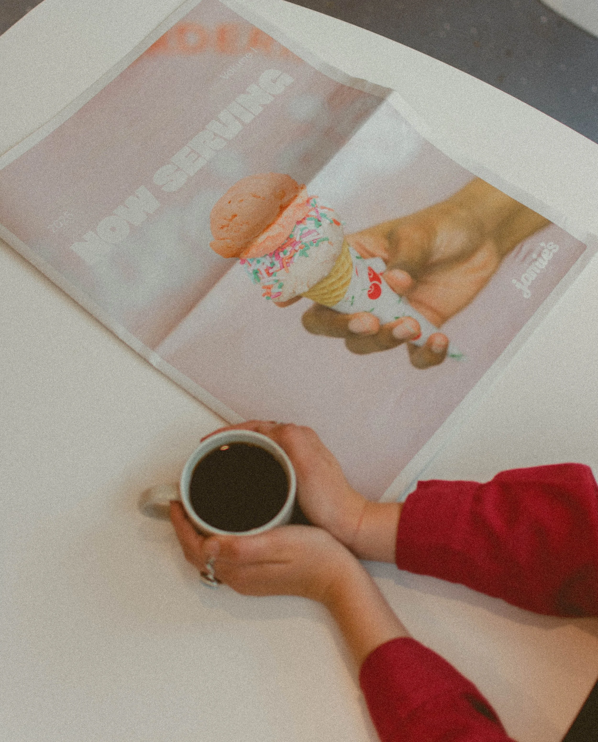 Person holding a coffee mug sitting at a table with a printed picture of an ice cream cone.