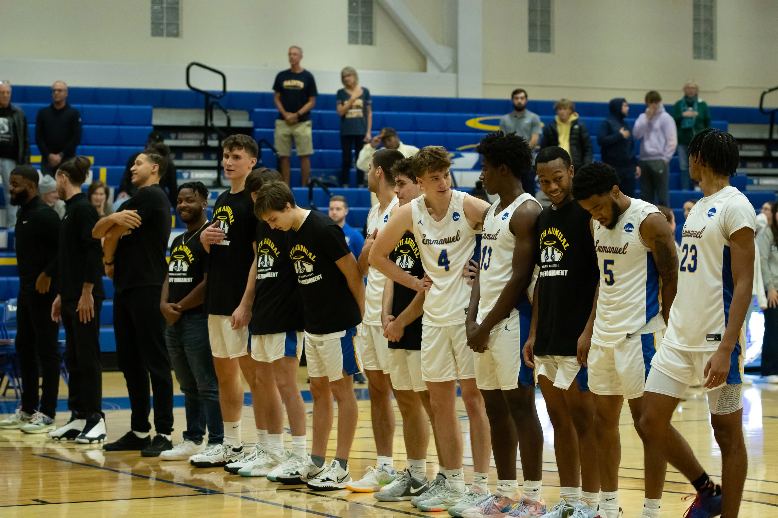A group of basketball players and spectators standing on a basketball court, lined up during a ceremony or event.