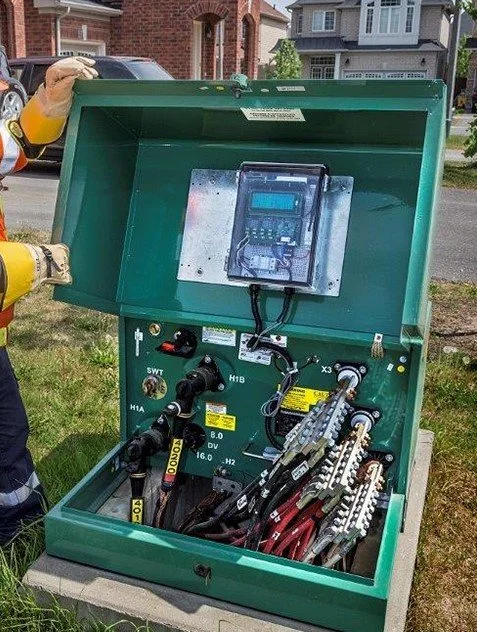 An outdoor electrical or telecommunications box with various connectors and equipment, being worked on by a person wearing gloves.