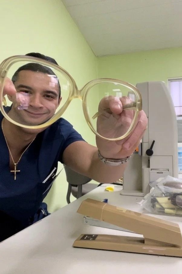 Person holding large round glasses in a room with office supplies and equipment.