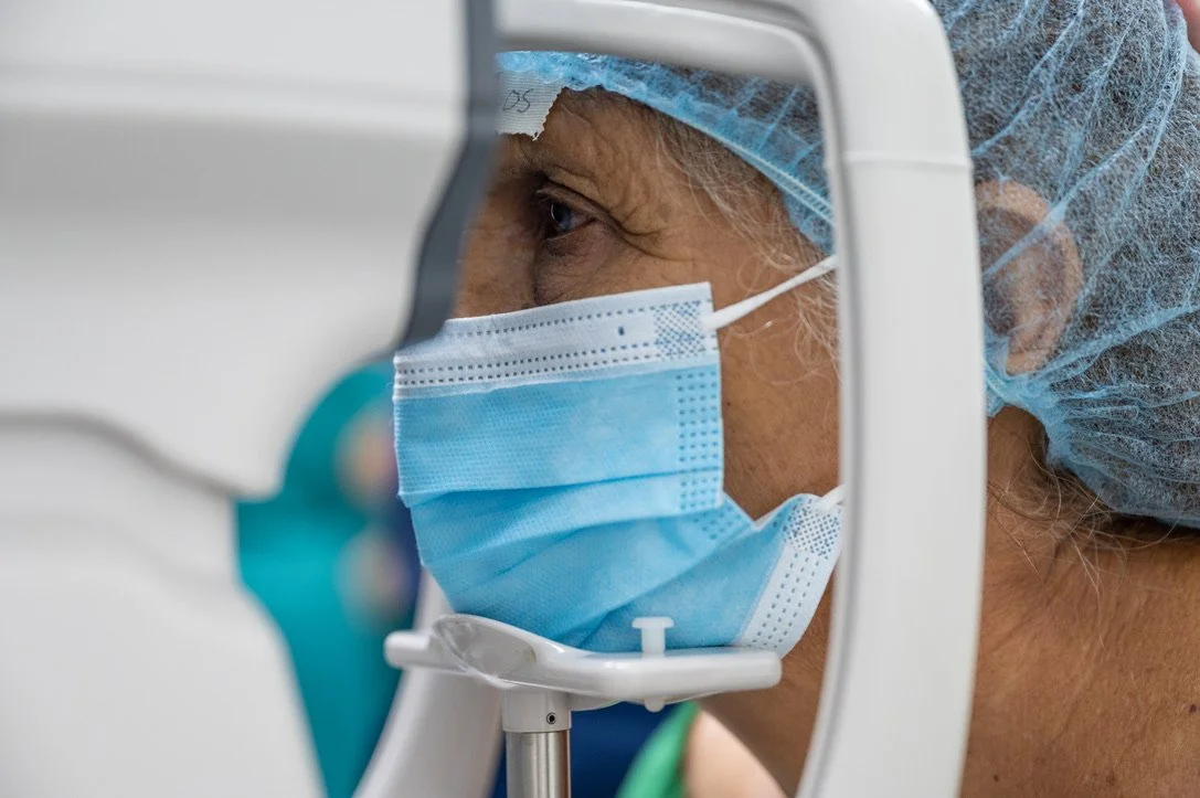 Person undergoing an eye examination wearing a face mask and head cover.