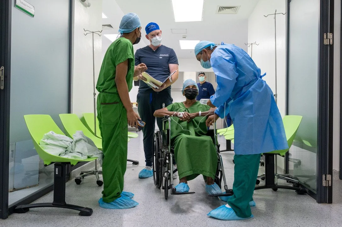 Medical professionals assisting a patient in a wheelchair in a hospital corridor.