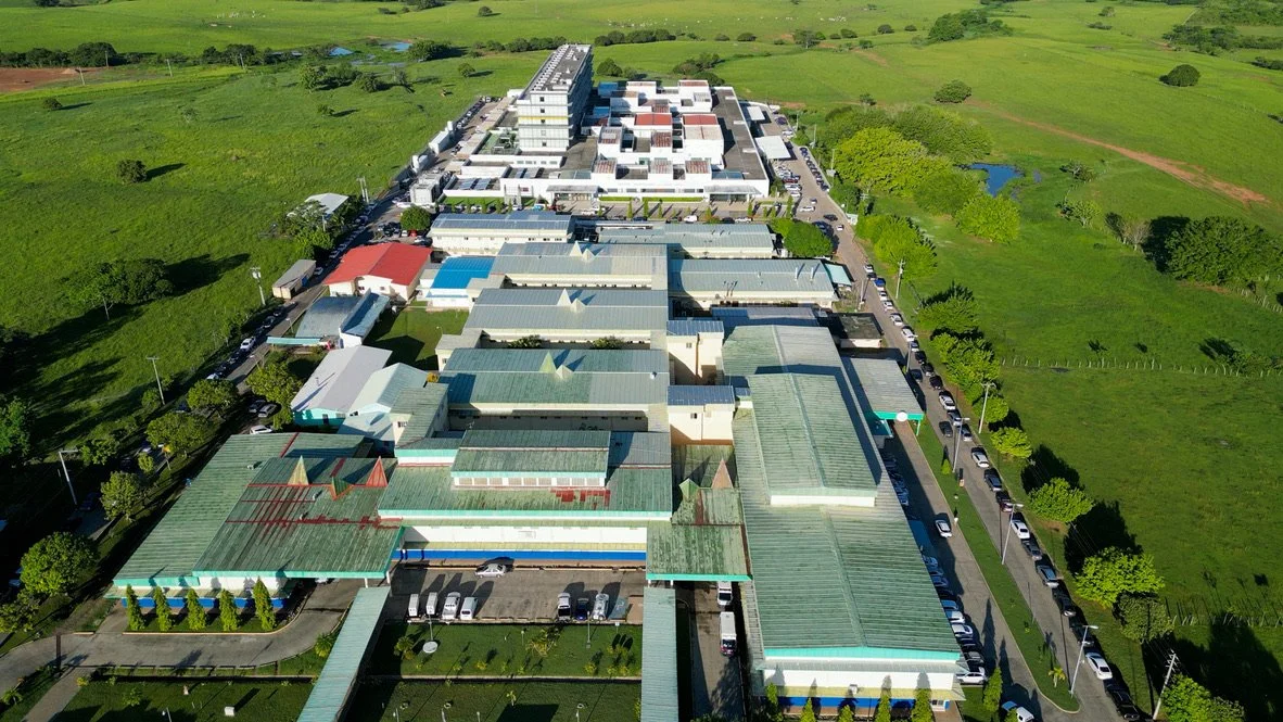Aerial view of a large hospital complex with multiple buildings surrounded by green fields and trees.