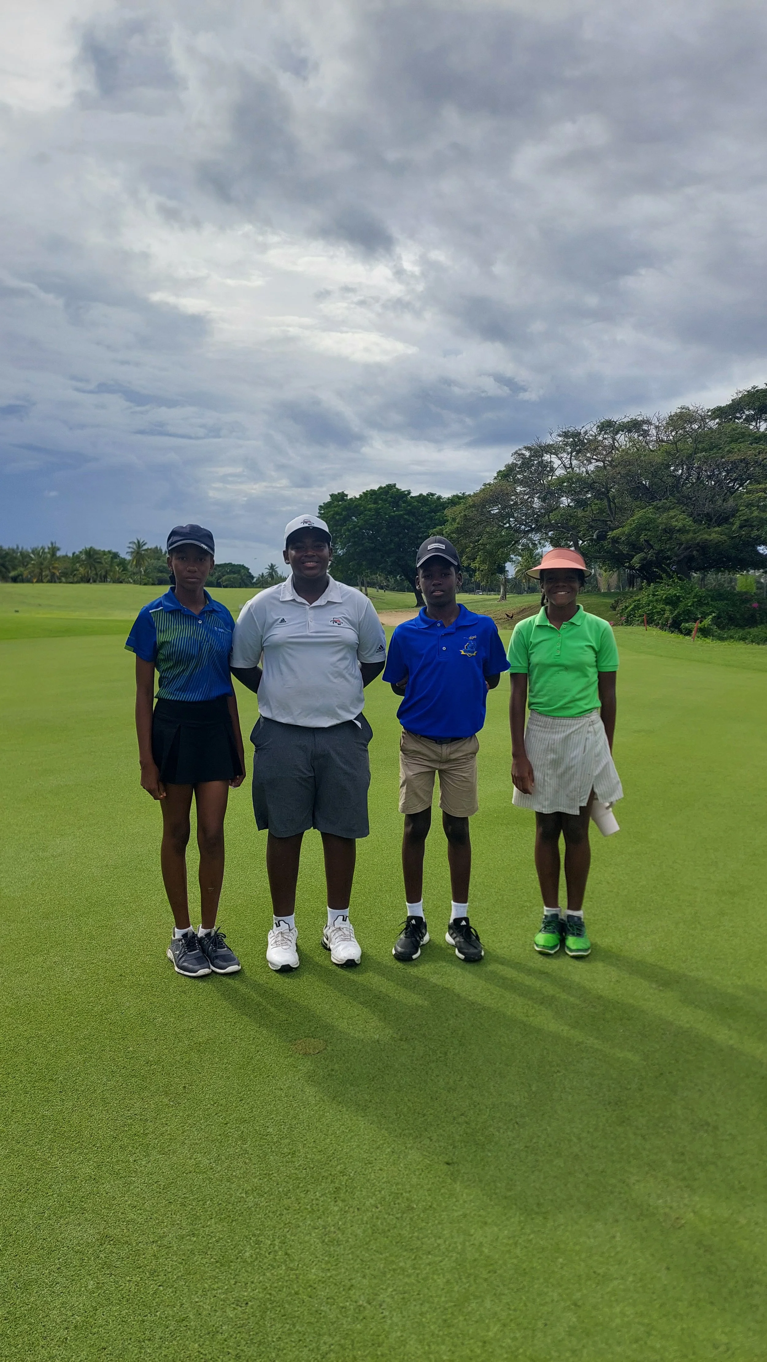 Four people standing on a golf course with cloudy sky in the background