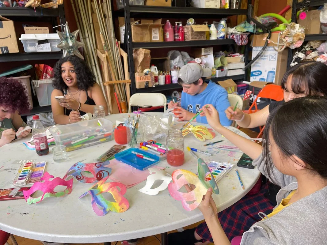 Group of people painting and decorating masks at a table in a craft room.