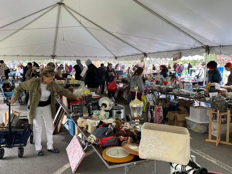 People browsing items at a flea market under a large tent with various objects on tables.