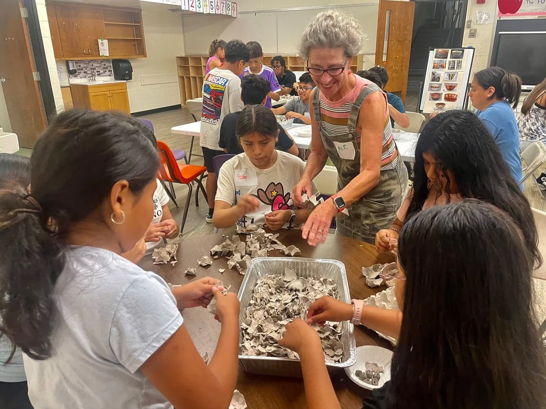 Children and teacher crafting at a table with paper materials in a classroom environment.