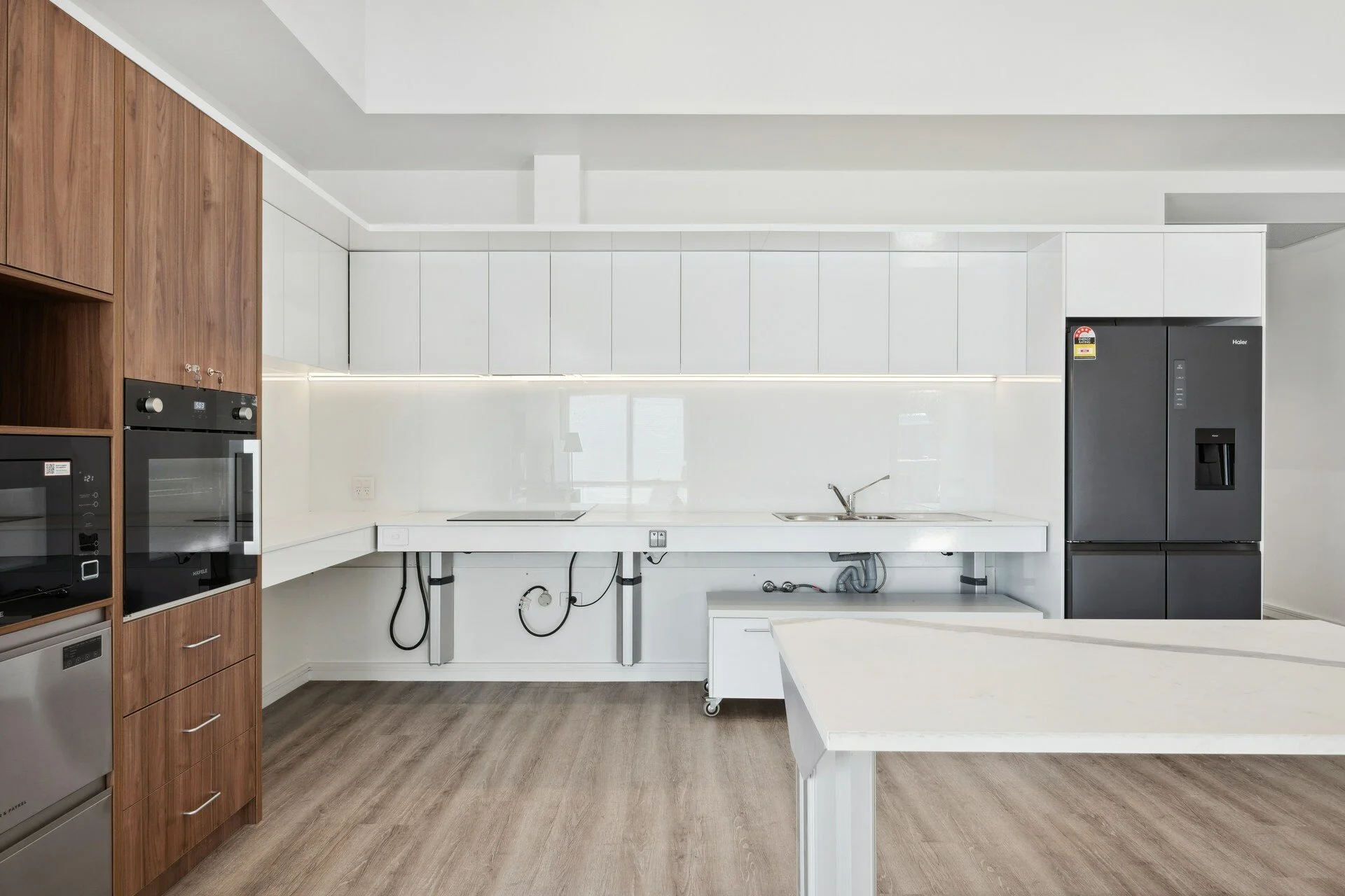 Modern kitchen with white cabinetry, black refrigerator, built-in oven and microwave, wood accents, and laminate flooring.