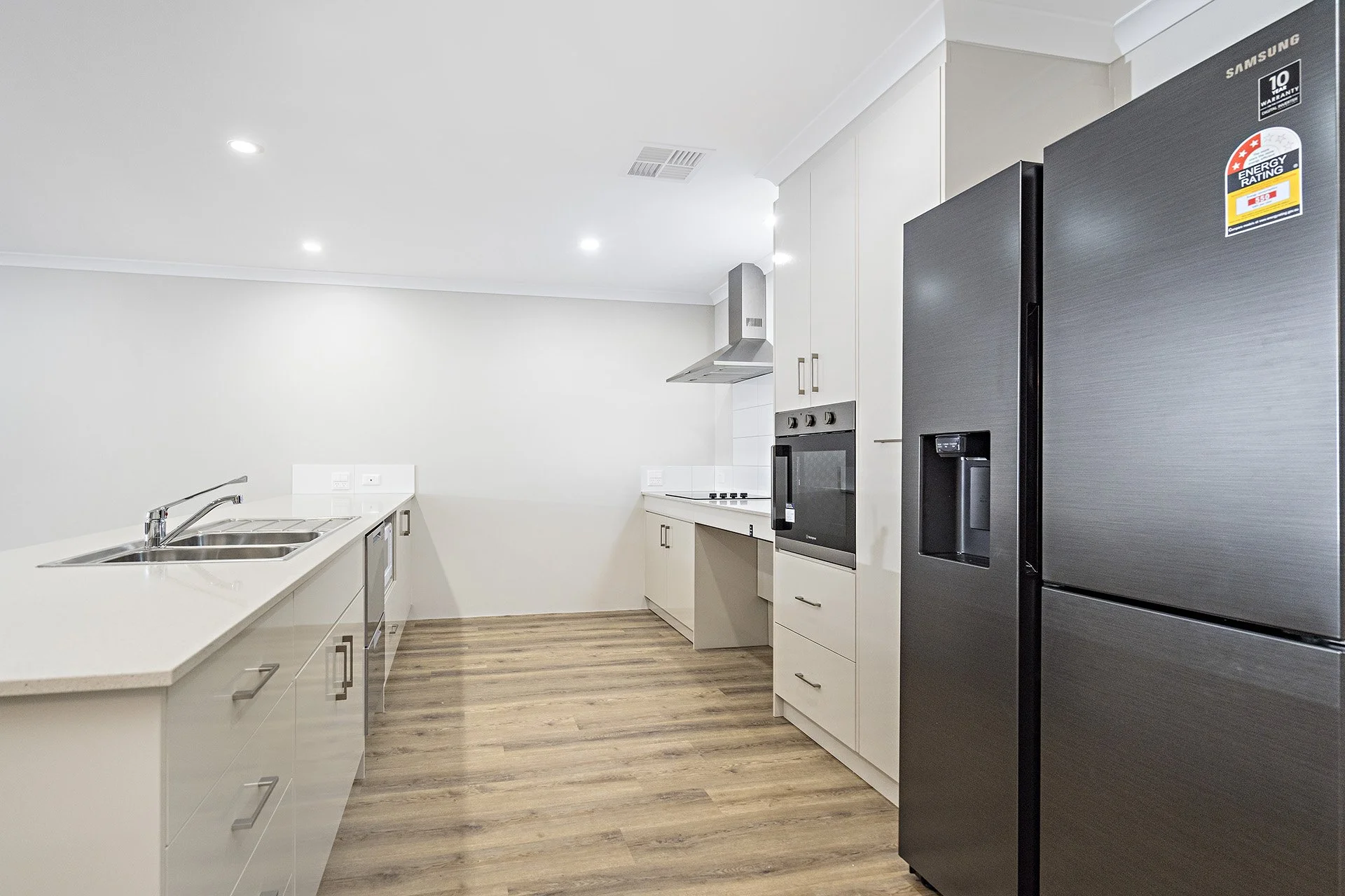 Modern kitchen with black refrigerator, stainless steel sink, oven, and range hood. Features ample cabinetry and hardwood flooring.