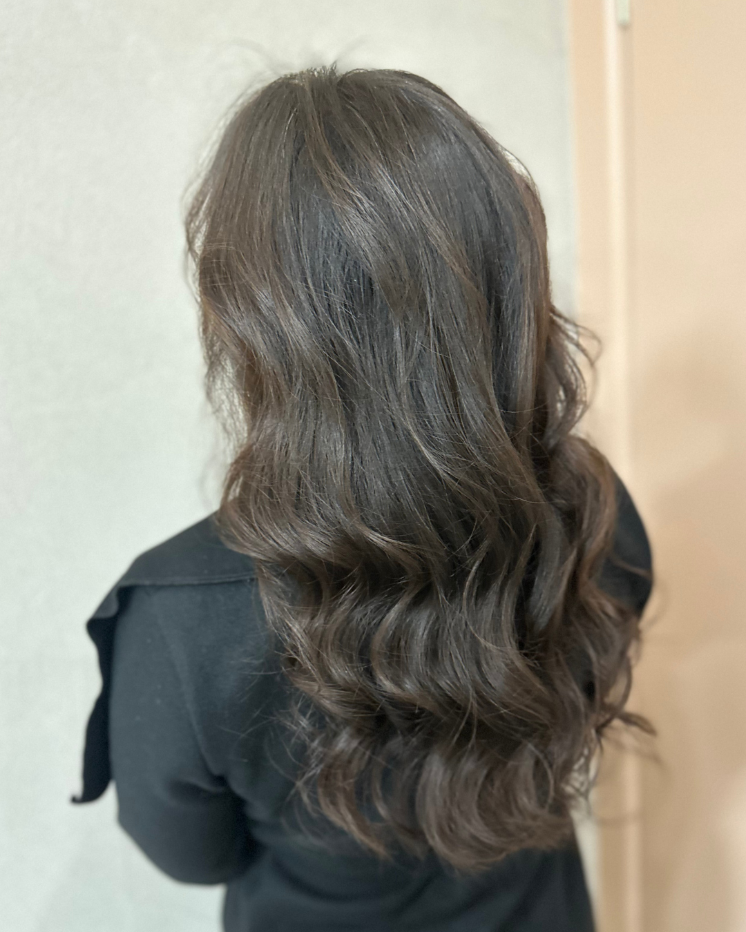 Back of a woman's head with shoulder-length, wavy brown hair, wearing a black top.