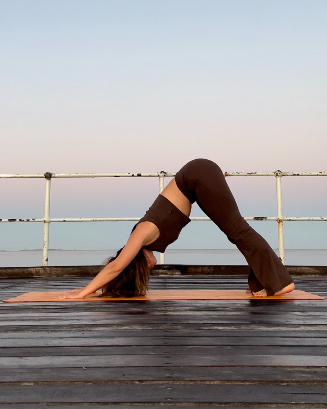 A woman practicing yoga in downward dog pose on a wooden deck outdoors during sunset.