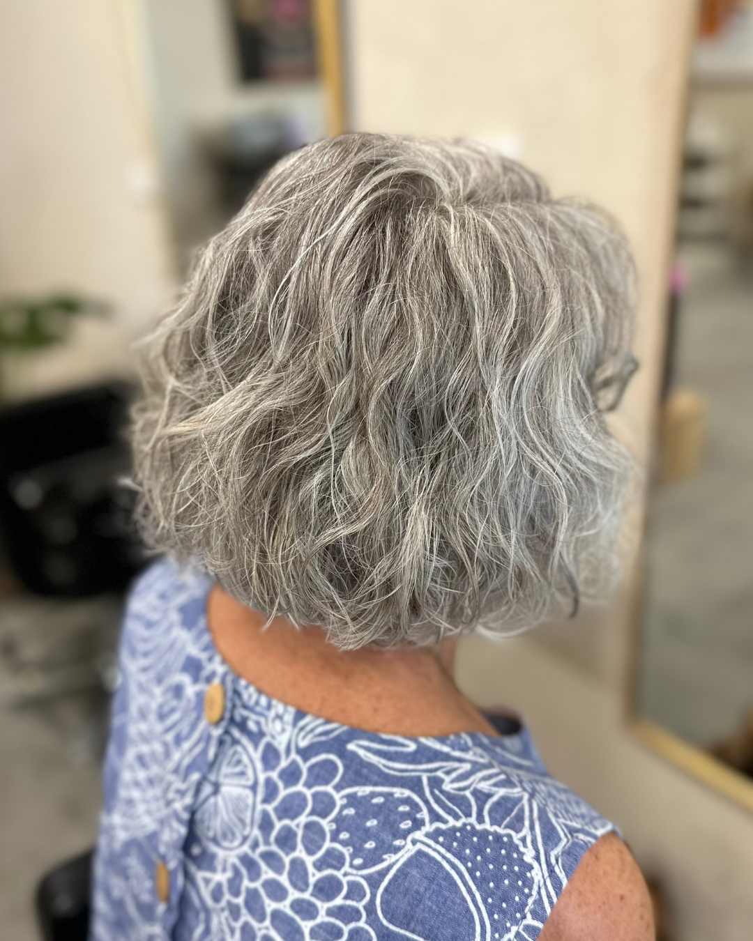 Back view of an elderly woman with short, curly, gray hair wearing a patterned blue and white sleeveless top.