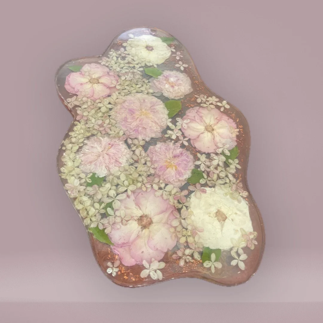 A decorative glass bowl filled with pink and white flowers and green leaves.