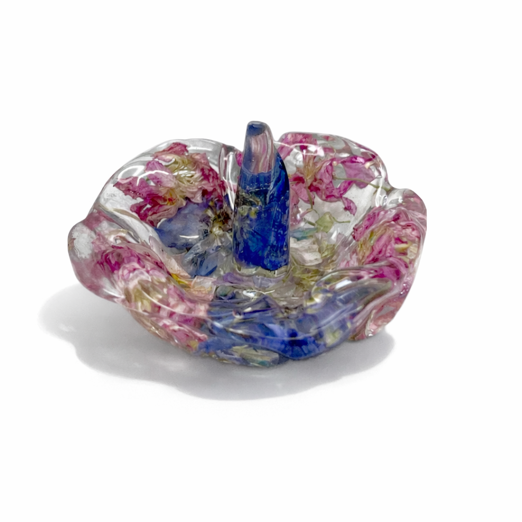 A colorful glass art sculpture resembling a flower with pink, blue, and purple hues against a white background.