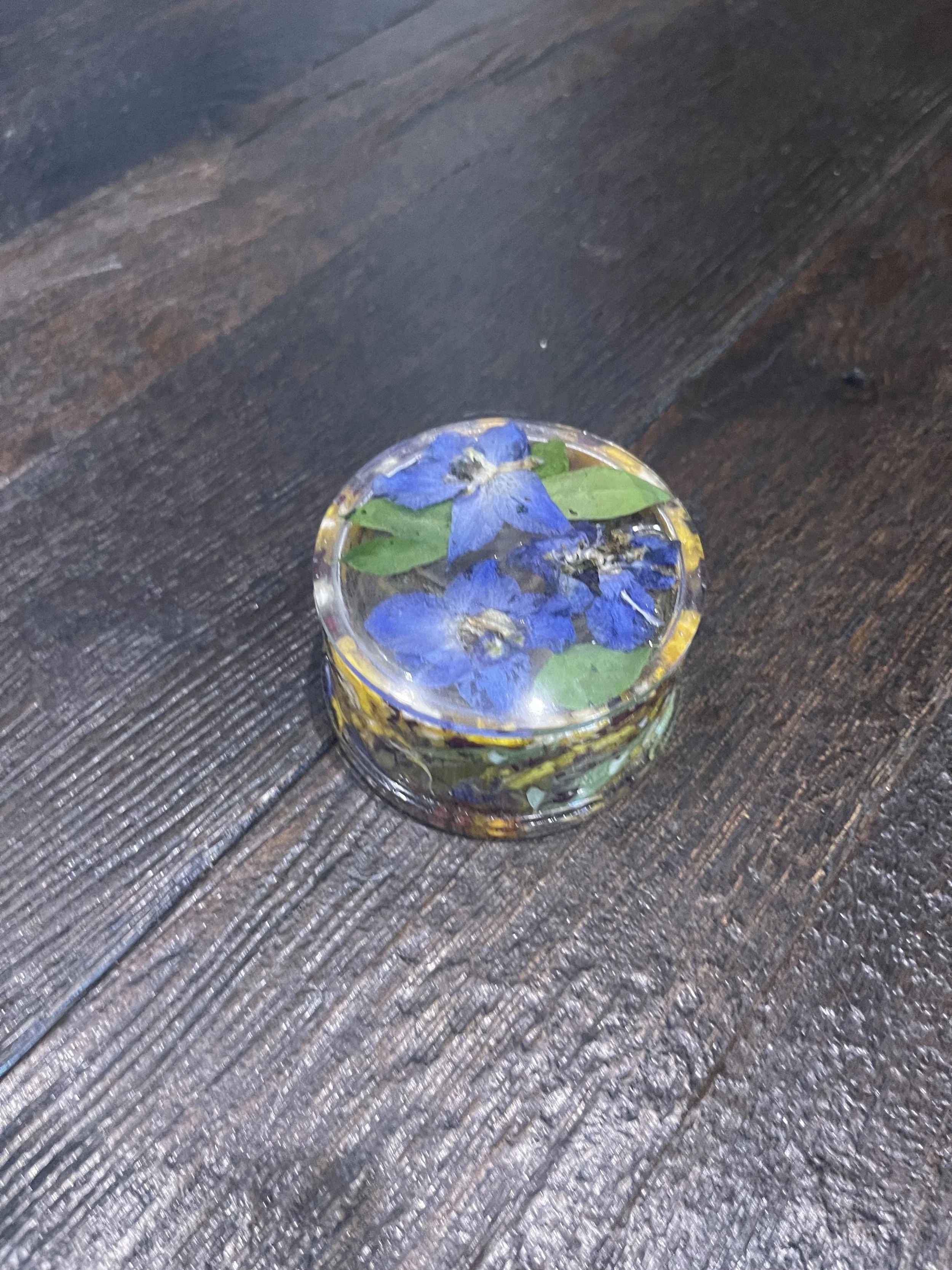 Glass bowl with blue flowers and green leaves submerged in water, placed on a wooden surface.
