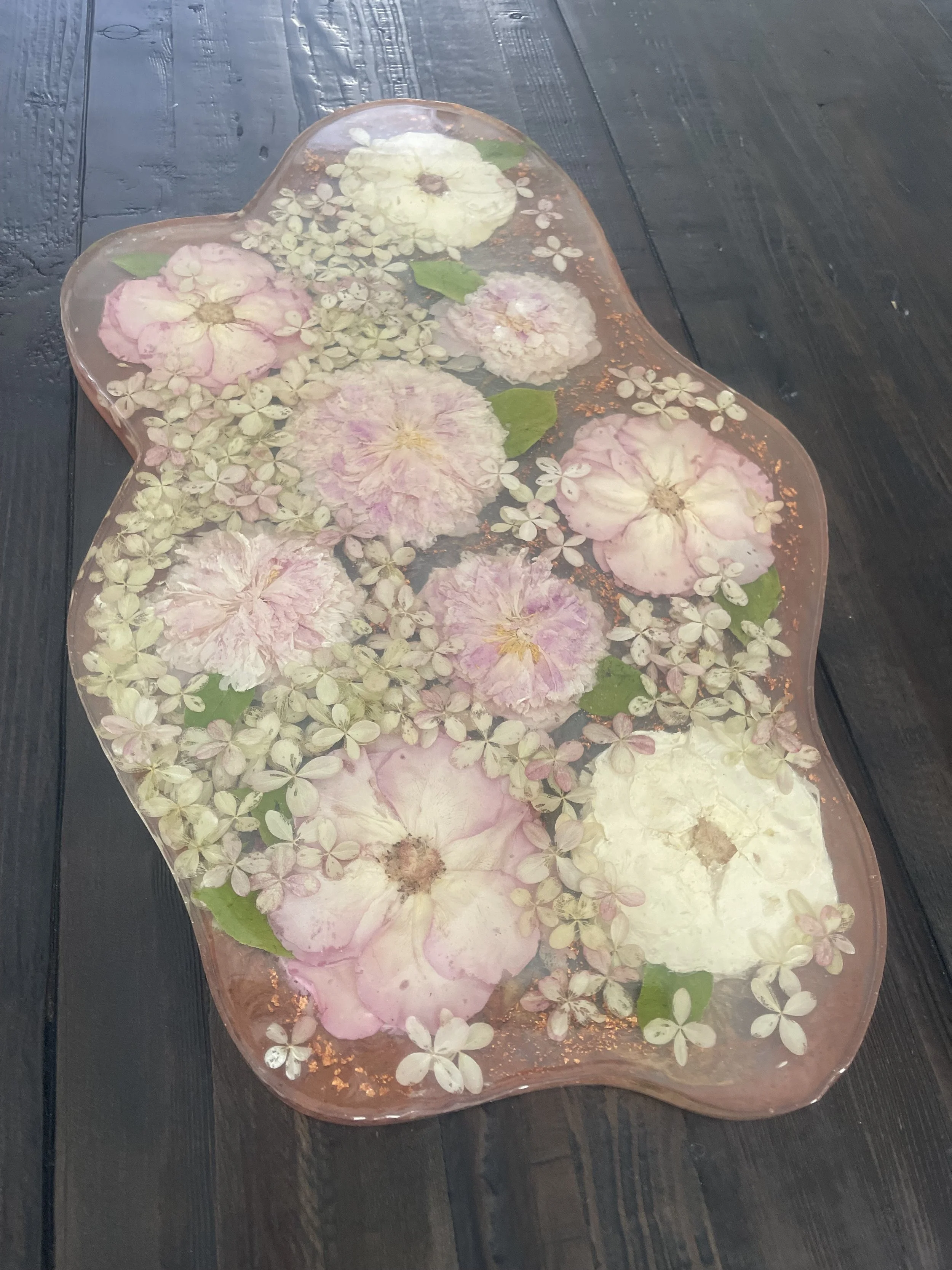 Decorative glass tray with pink and white hydrangea flowers and green leaves on a dark wooden surface.