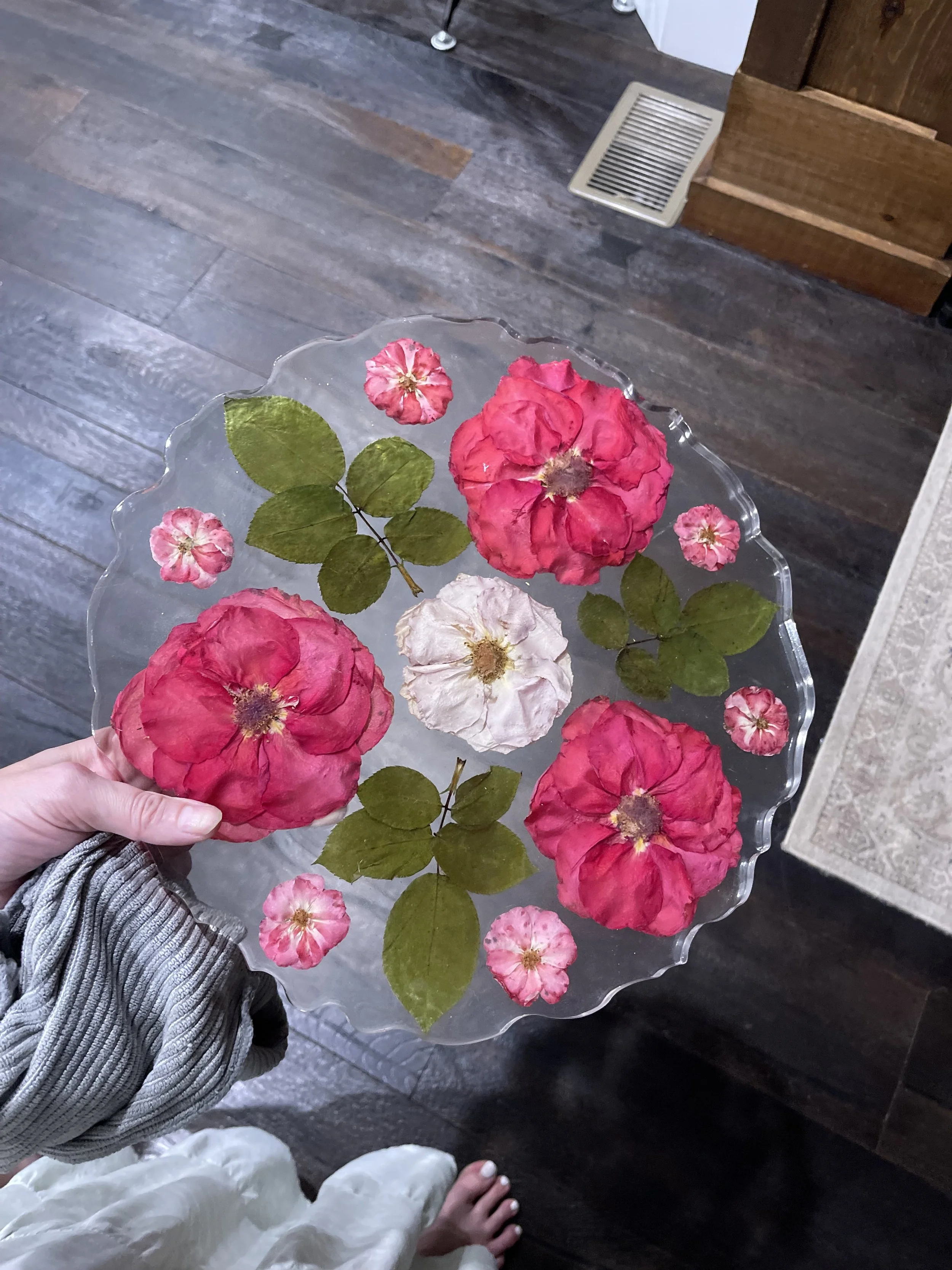 Hand holding a glass plate with pink and white flowers and green leaves arranged on it
