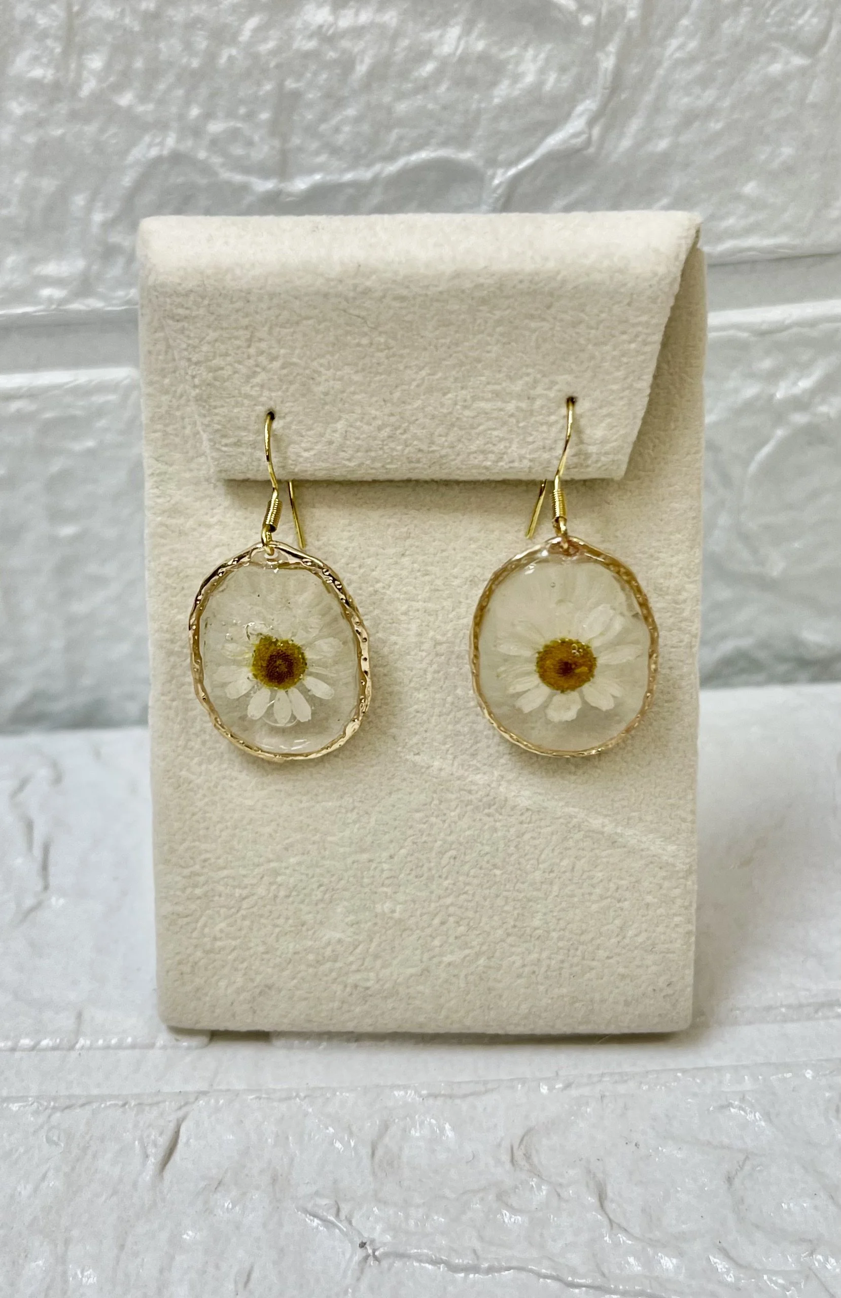 Daisy flower earrings with gold frames displayed on a beige jewelry card.