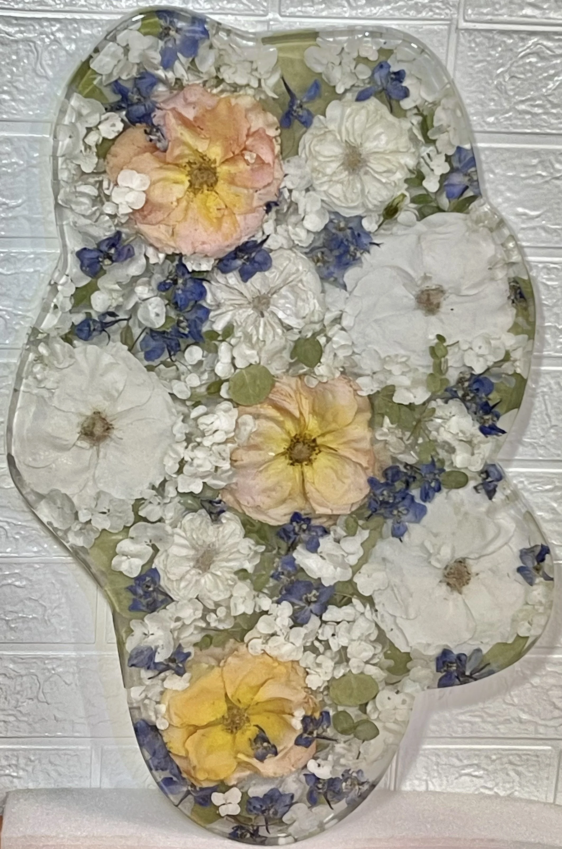 Decorative glass floral arrangement with white, pink, yellow, and blue flowers on a white textured background.