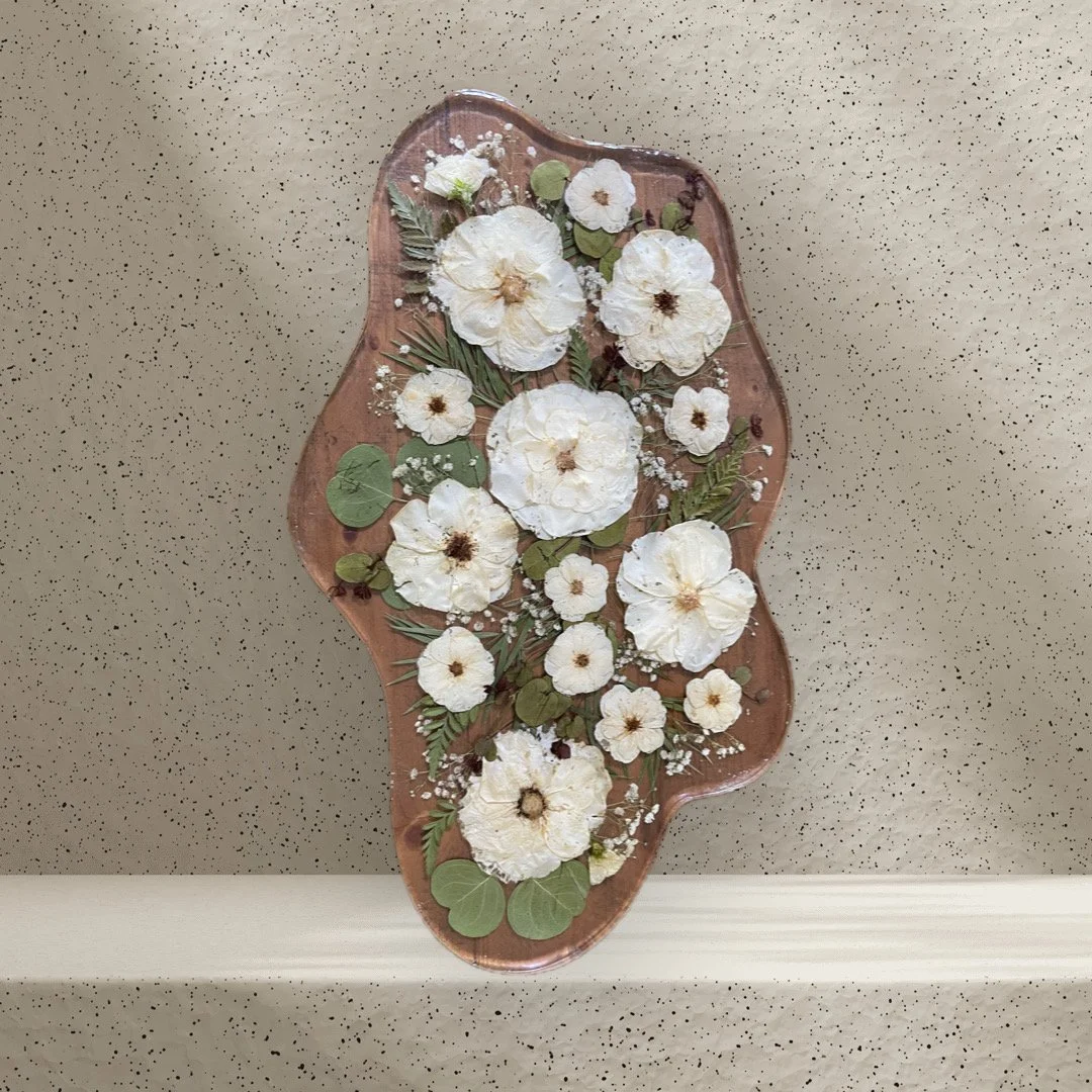 Decorative wooden tray with white pressed flowers and green leaves.