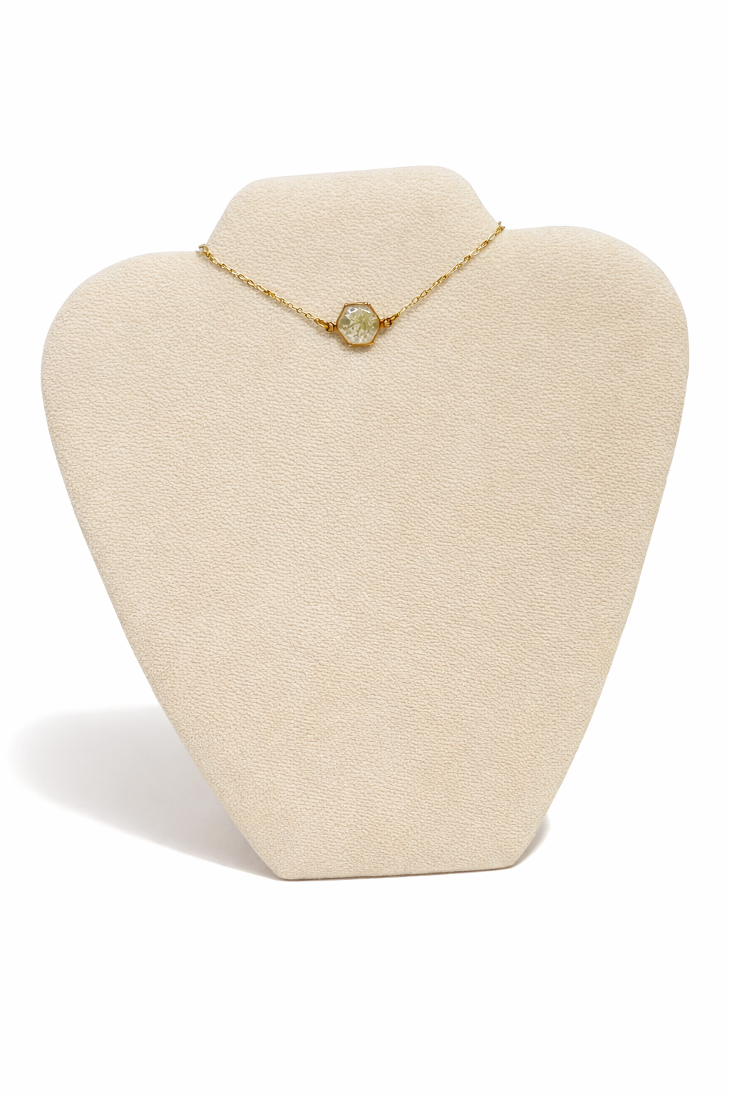 Gold necklace with a hexagon-shaped pendant showcasing a white floral design, displayed on a beige jewelry stand.