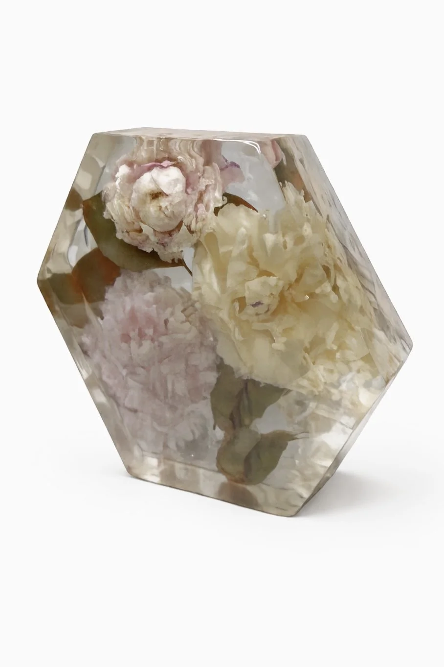 A transparent, faceted, hexagonal-shaped container with dried flowers inside, including a white rose and pink peony.