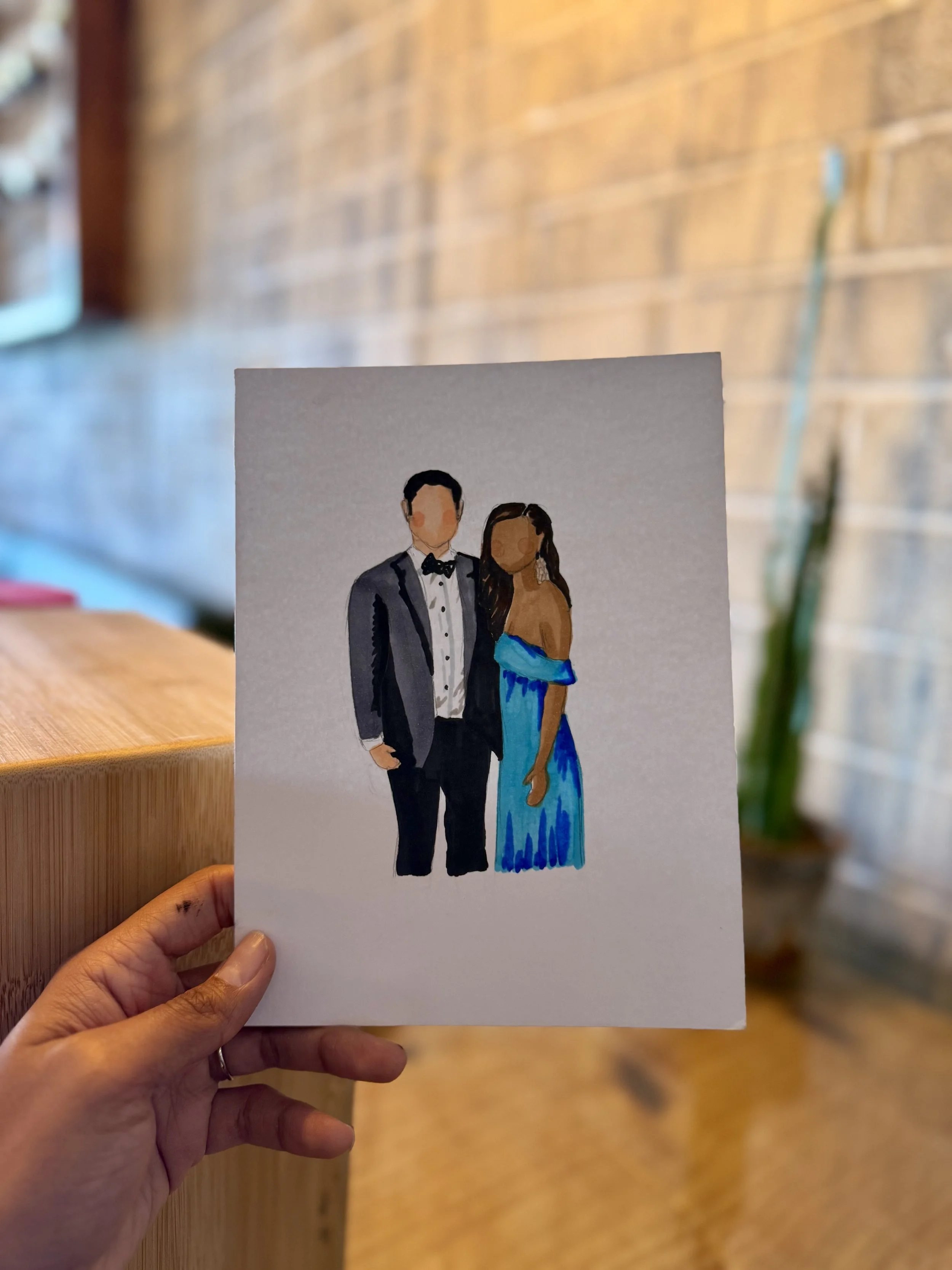 A hand holding a portrait of a couple dressed in formal attire against a blurred indoor background.