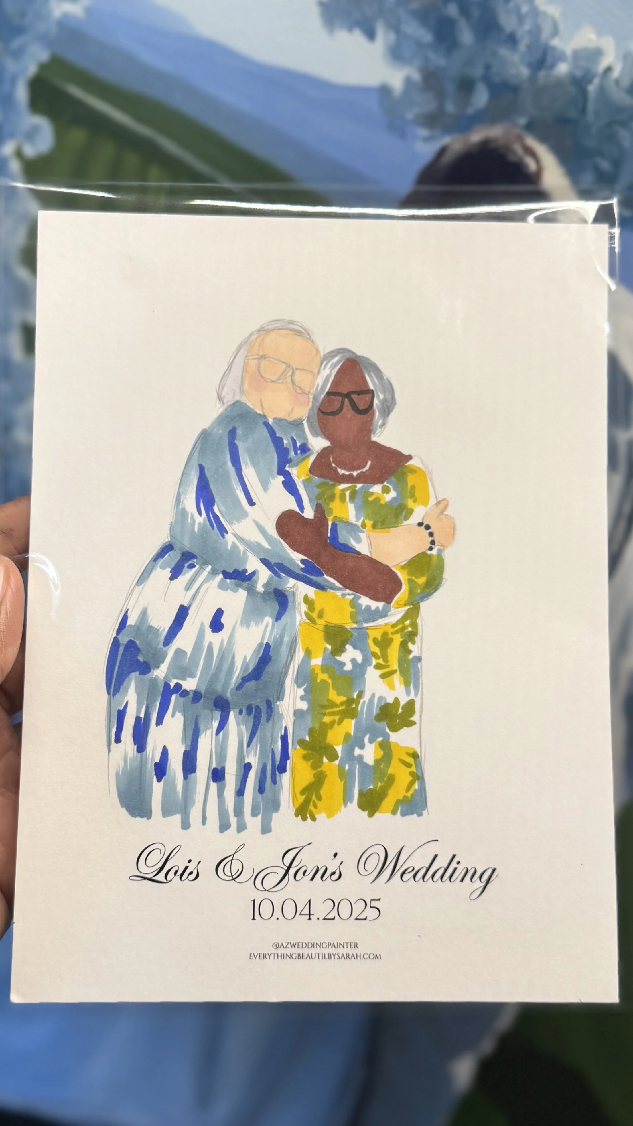Illustration of two women, one with light skin and gray hair wearing glasses and a blue dress, and the other with dark skin and gray hair wearing glasses and a yellow floral dress, embracing at a wedding. Text reads "Lois & Jon's Wedding" with date 1