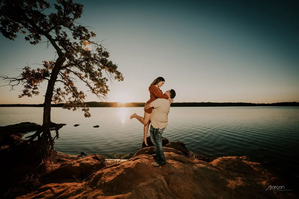 An engaged couple sharing a joyful moment beside the lake at sunset