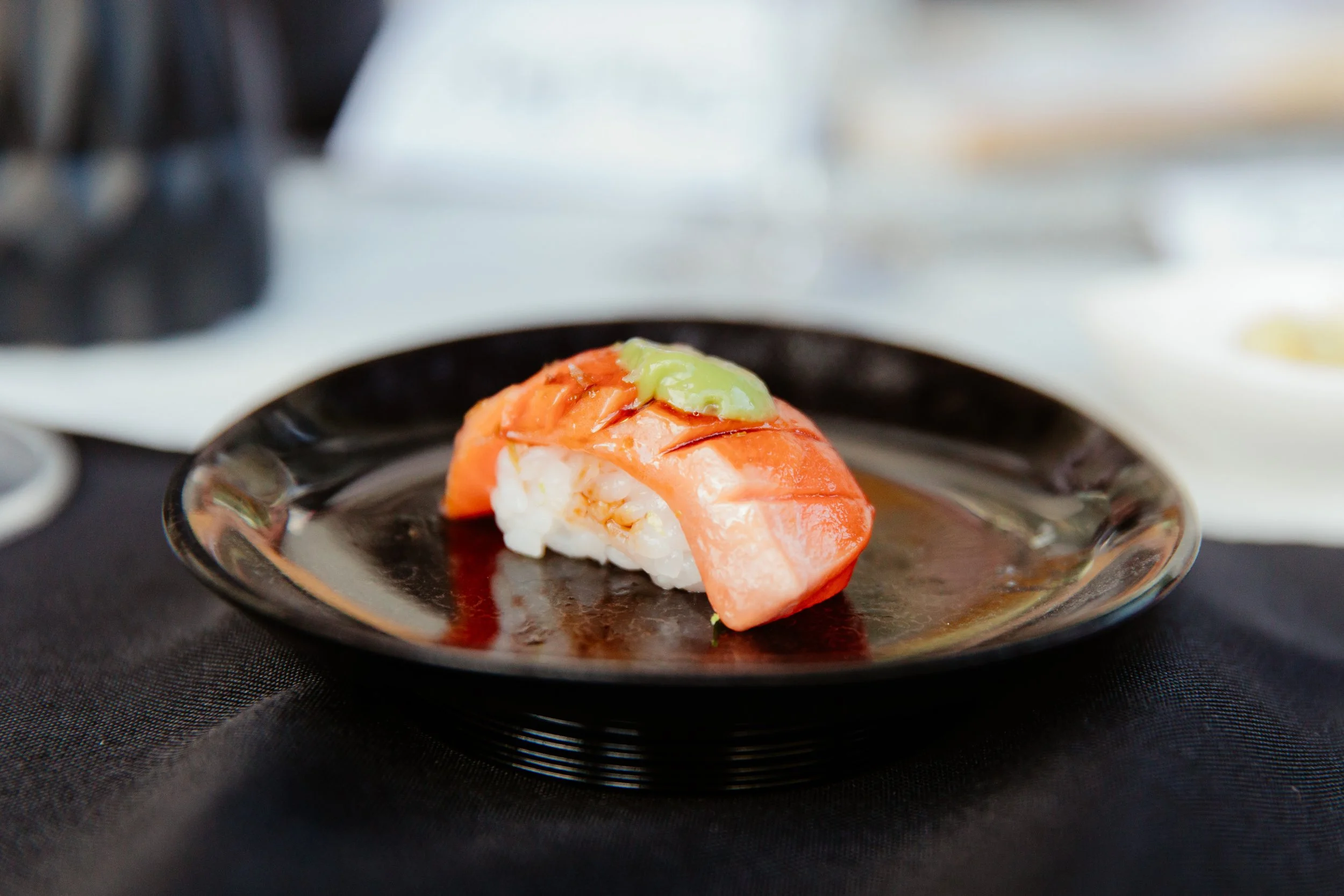 A piece of sushi with shrimp, avocado, and rice served on a black dish.