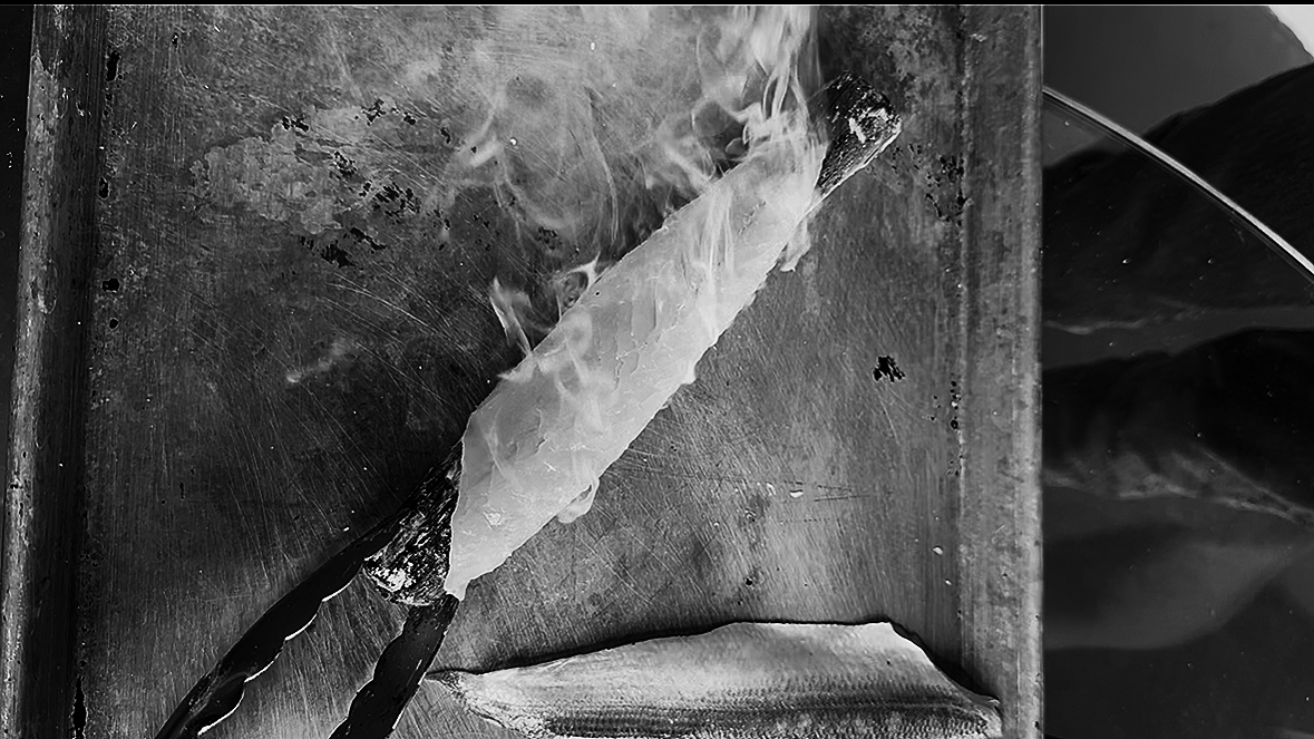 A piece of paper or tissue being burned on a metal surface, with smoke rising from the flames.