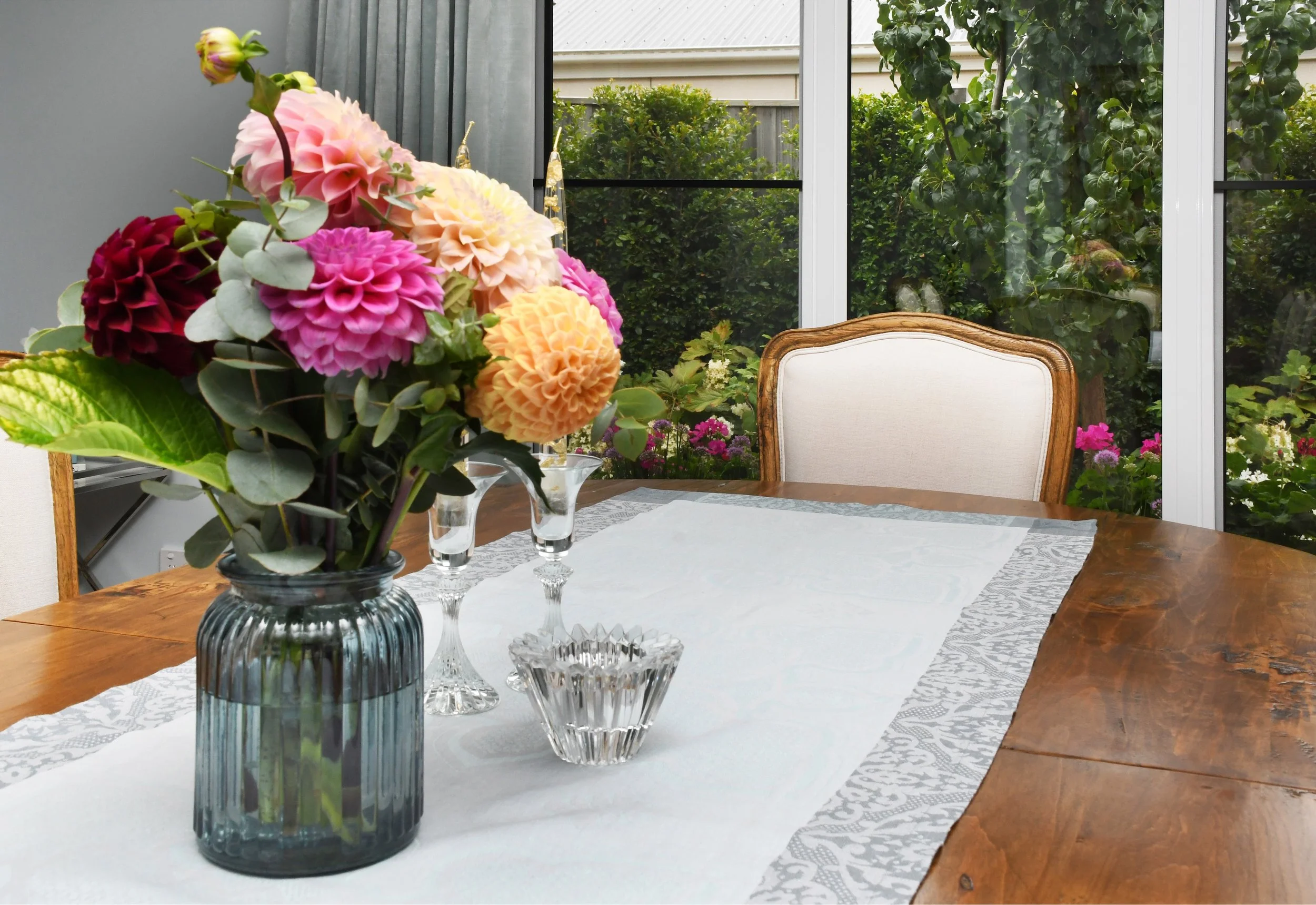 French style oak dining setting with duck egg blue runner and dahlia flowers in pink, apricot and yellow alongside three crystal candlesticks
