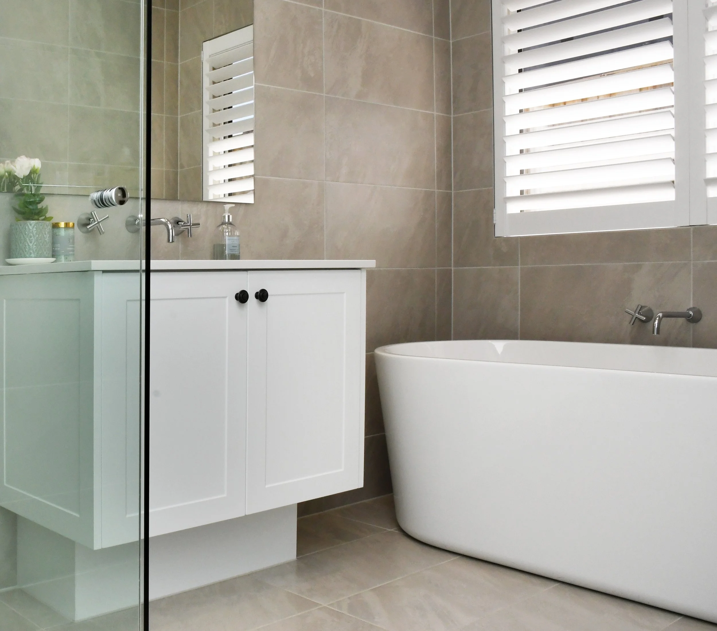 Cloudview bathroom with white shaker style vanity, under mount sink and chrome tap ware to offset the large mirror and freestanding white bath. A light and airy space with taupe stone floor to ceiling tiles.