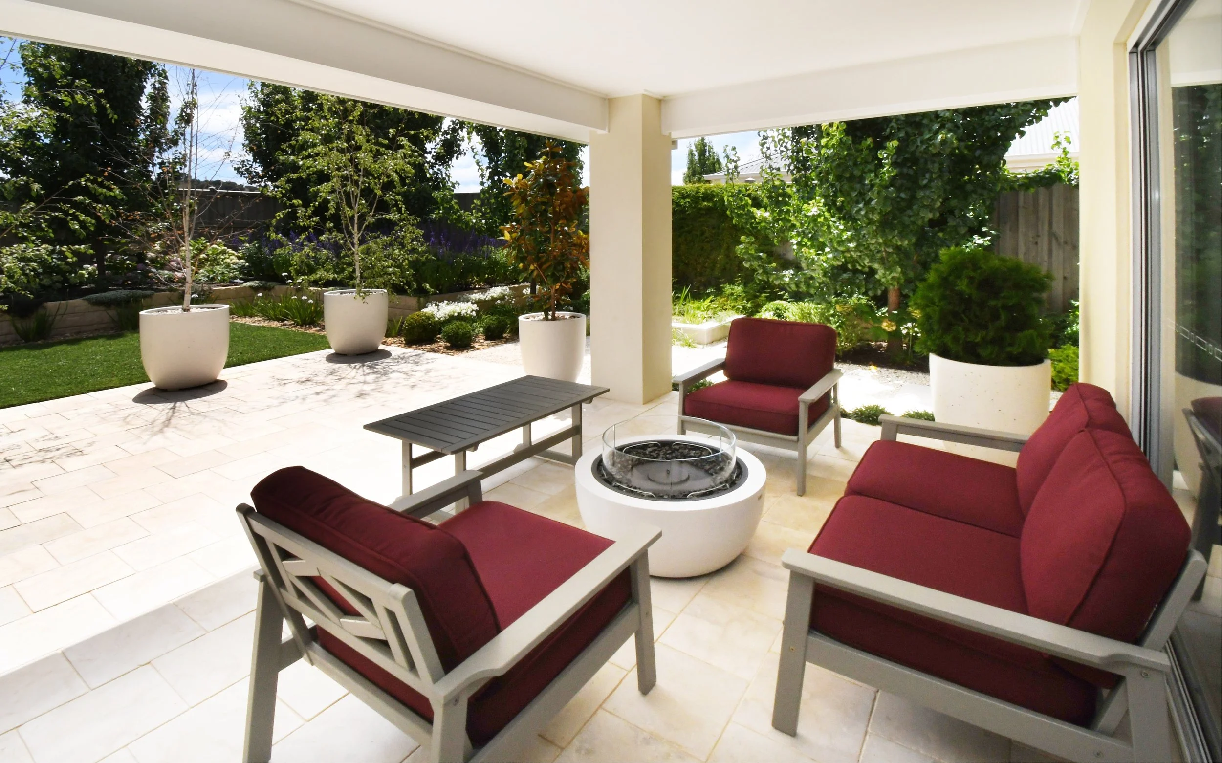 Cloudview alfresco area featuring cream marble stone paving, grey and burgundy lounge chairs and an ethanol fire pit, looking towards the beautiful deep green of the north facing garden.