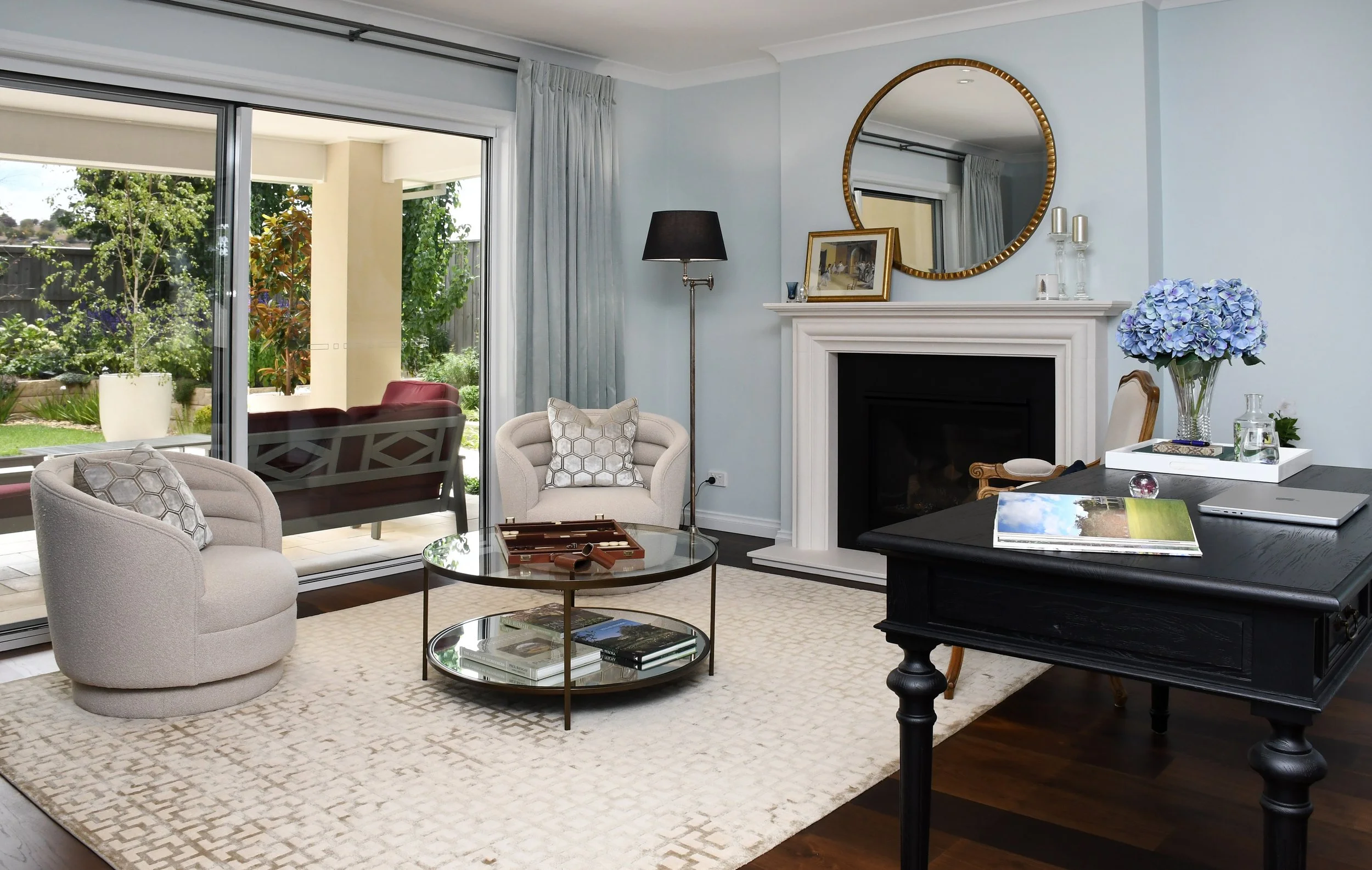 Interior view of Cloudview living room featuring oak flooring, a cream rug, cream tub chairs and a classic limestone fireplace creating a peaceful space to chat or read by the fireside.