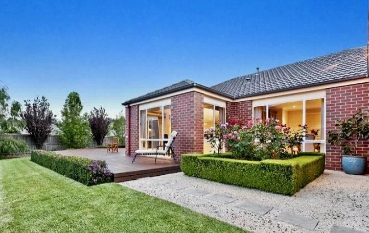 The rear garden at the Georgian Home features a large entertaining deck in merbau timber with a hedged rose garden and hebes to complement its geometric lines.  A lush green lawn pathway sits between the gravel walkways and deep garden beds filled wi