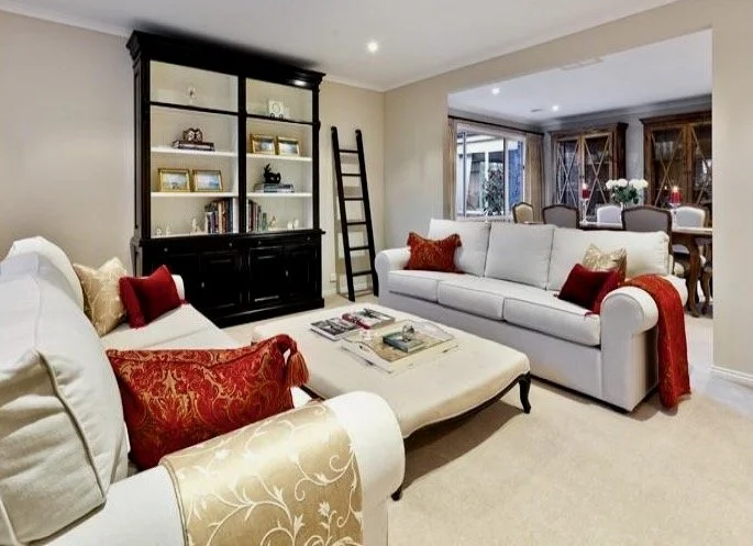 The rich colours of gold and red tapestry in the feather down cushions and throws on deep cream linen sofas offer an elegant place to sit and relax in the Georgian Home living room. A large black and white library bookcase shows off books and family 