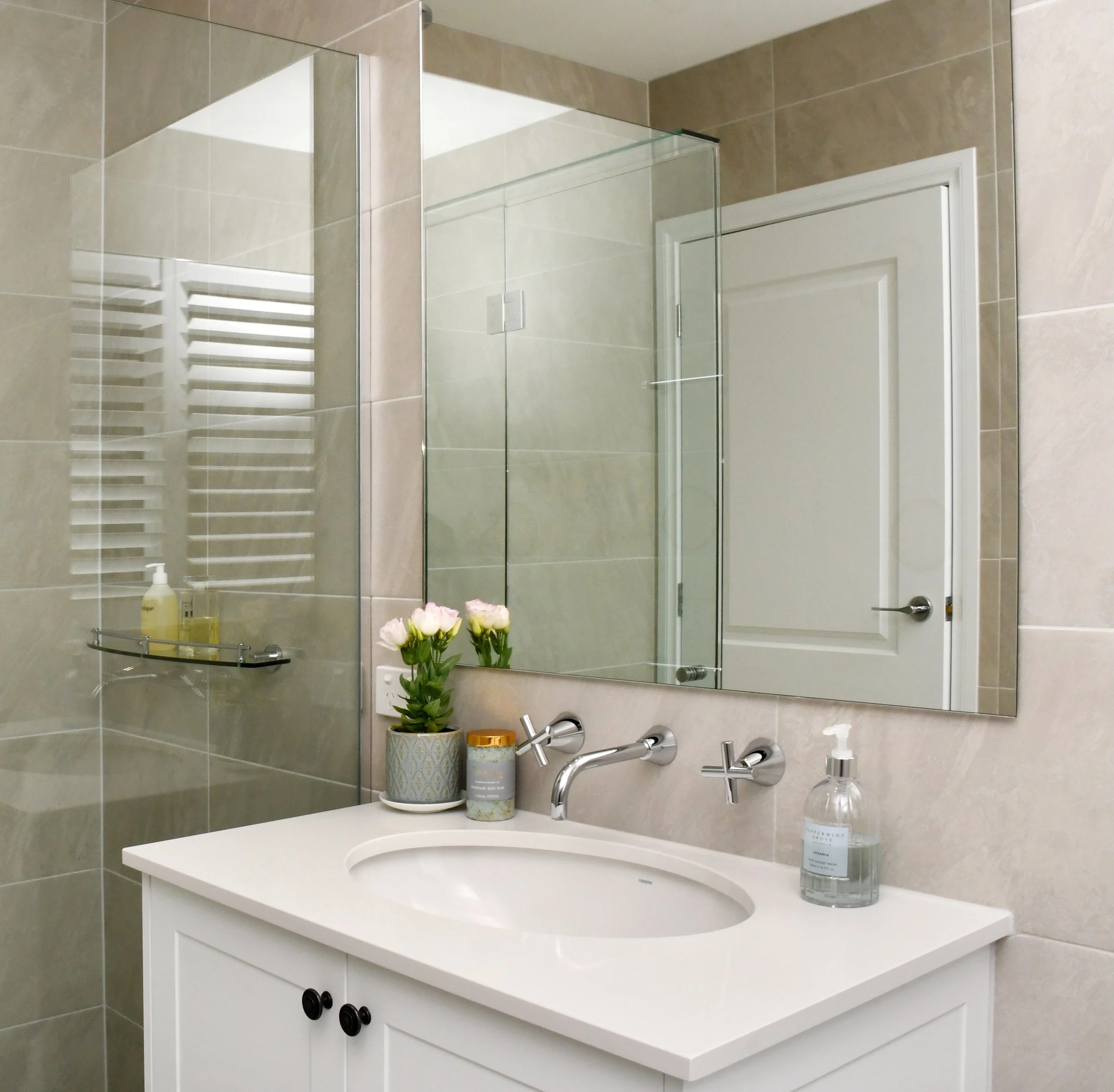 Cloudview bathroom with white shaker style vanity, under mount sink and chrome tap ware to offset the large mirror and frameless glass shower. A light and airy space with taupe stone floor to ceiling tiles.