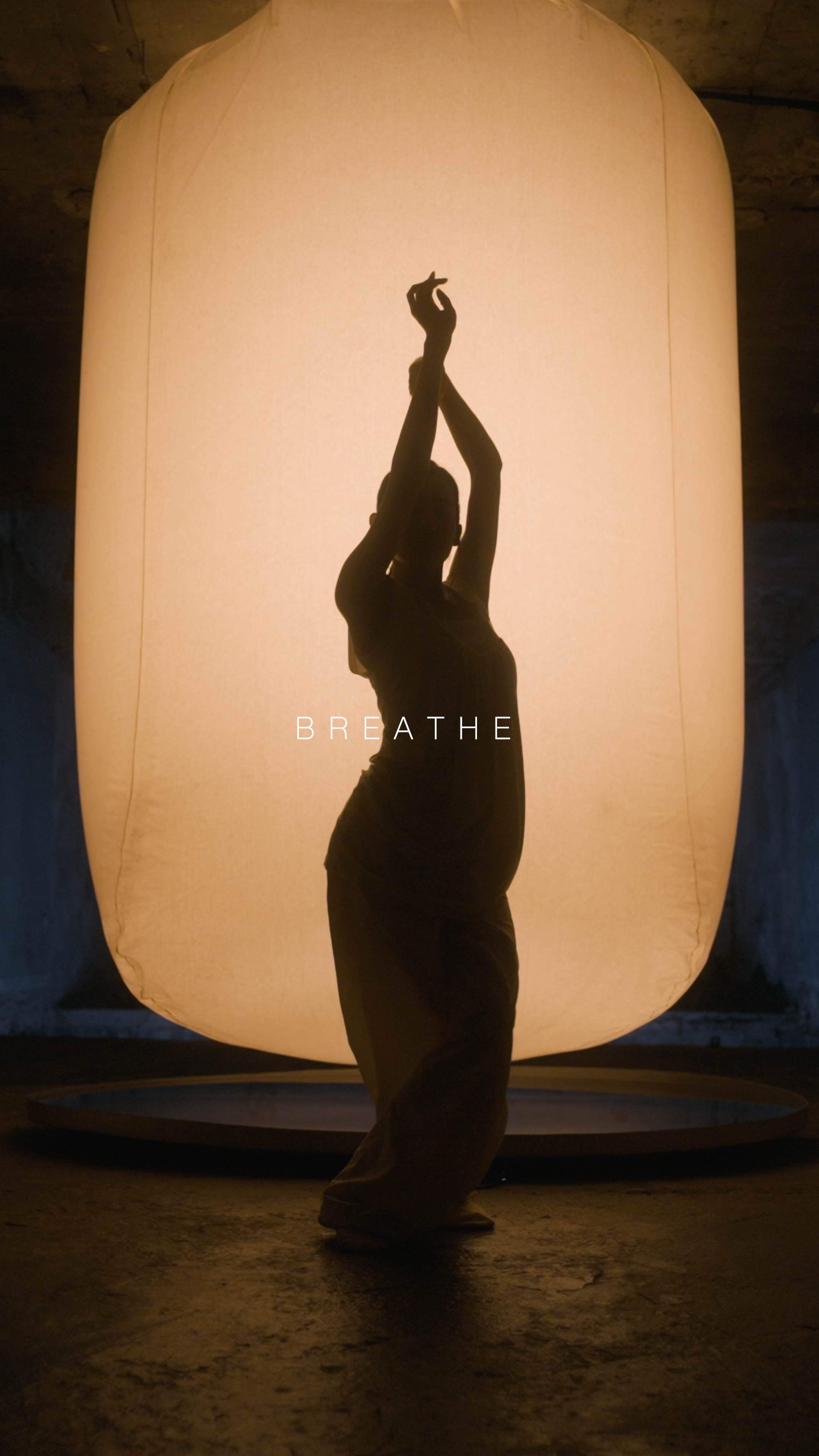 Silhouette of a person dancing in front of a large illuminated lantern with the word "BREATHE" written across it.