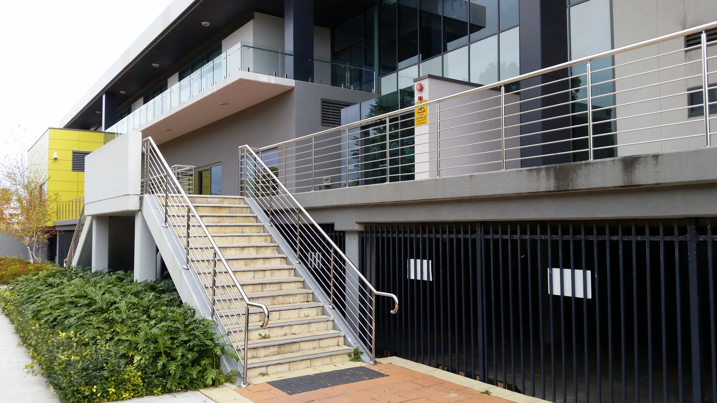 Modern multi-story building with exterior staircase and metal railings, surrounded by greenery
